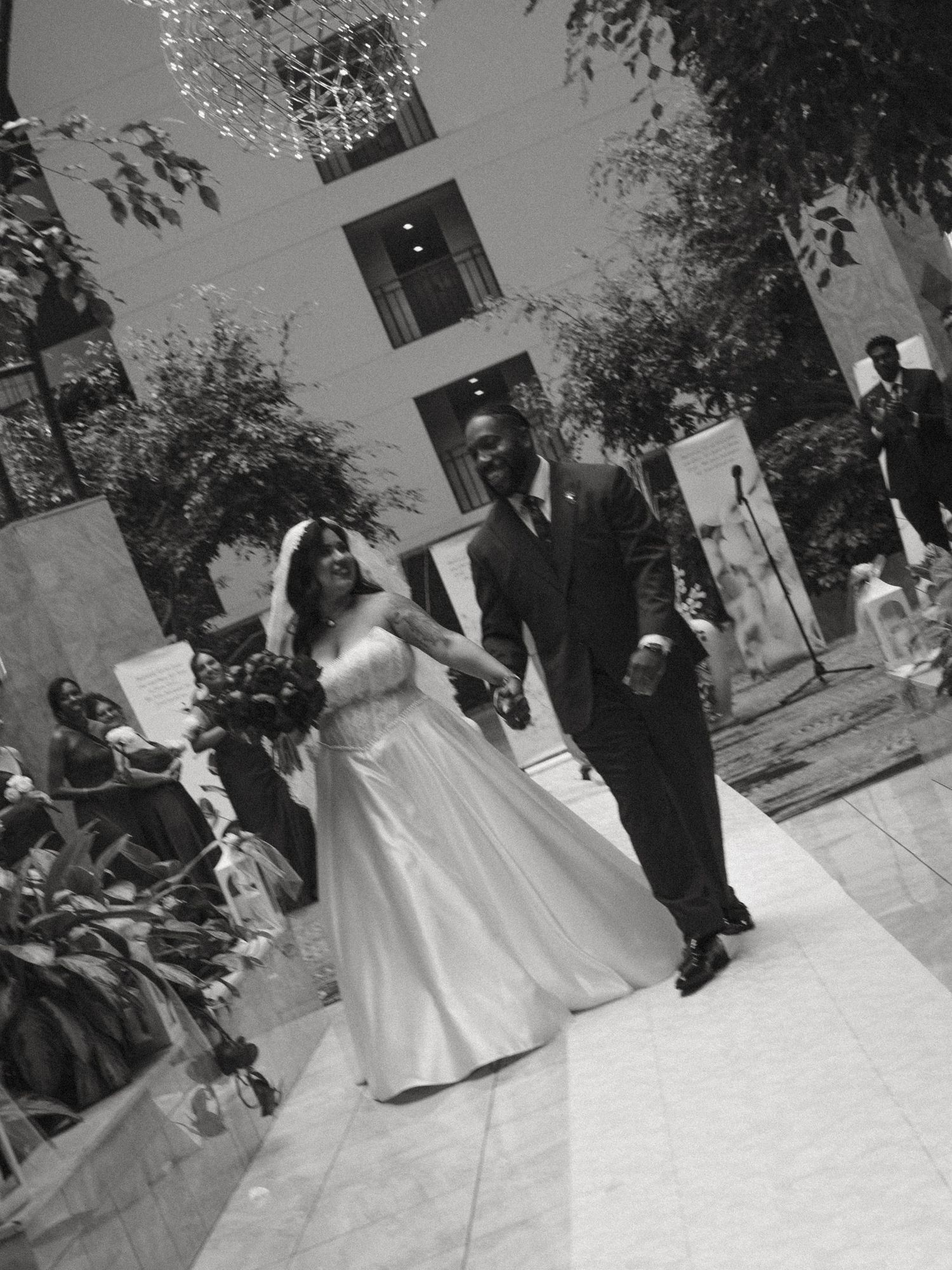 Black and white photo of newlyweds holding hands walking back down the aisle after their wedding ceremony.