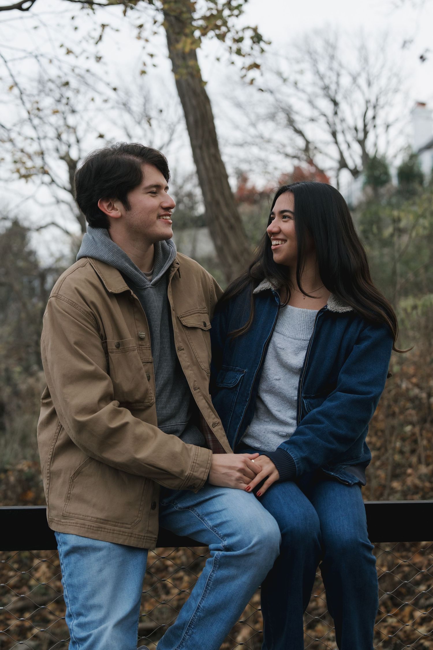 A smiling young couple holds hands while sitting on ledge in an autumn park.