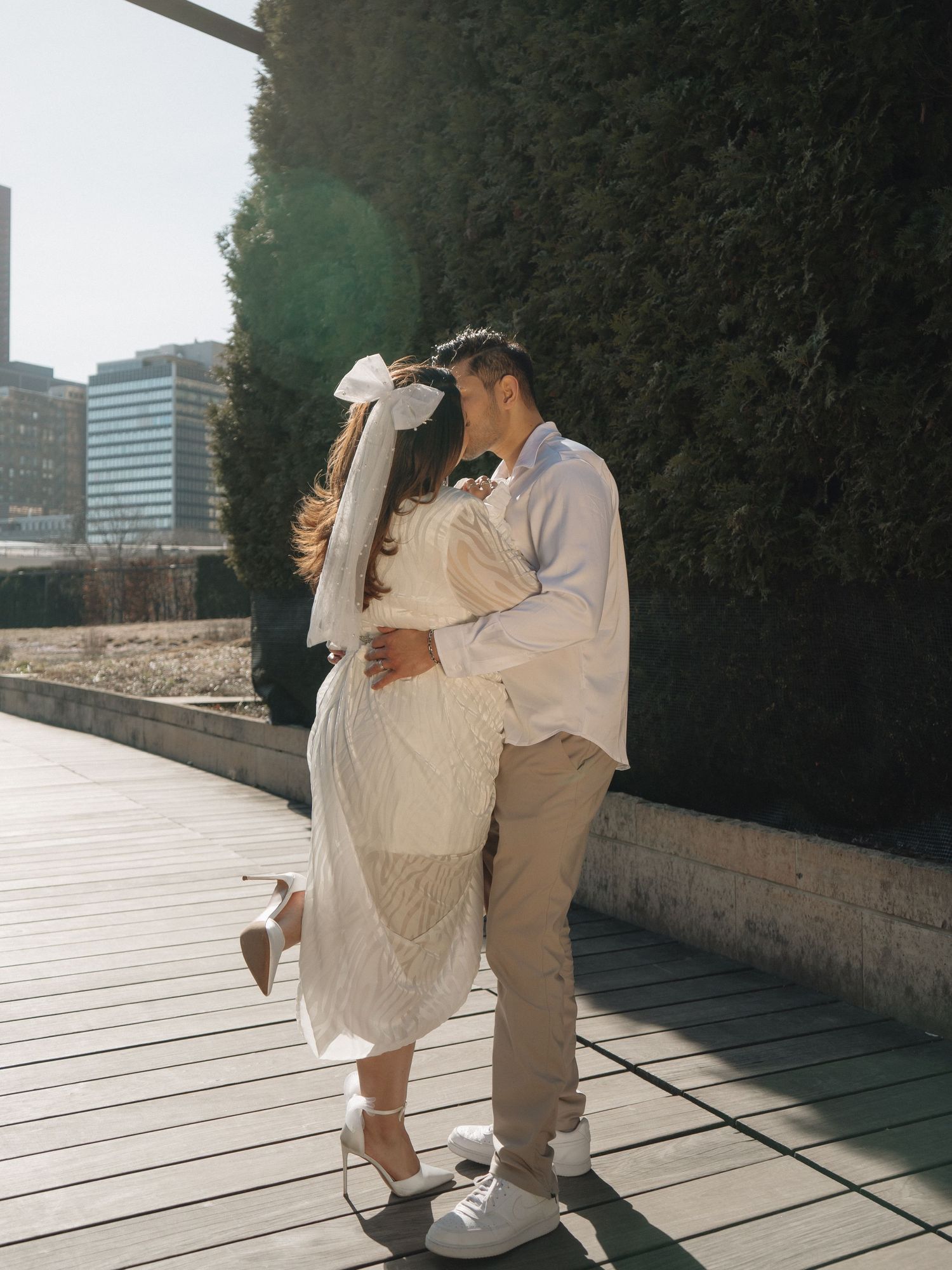 Couple kissing in sunlight on a wooden walkway, bride wearing white dress and hair bow.