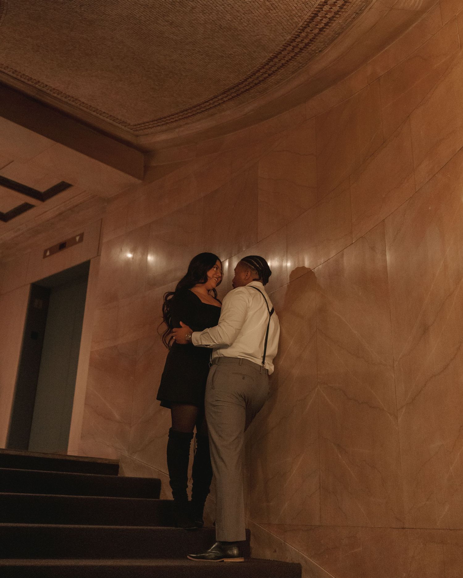 Romantic couple sharing a kiss on dimly lit ornate building staircase.