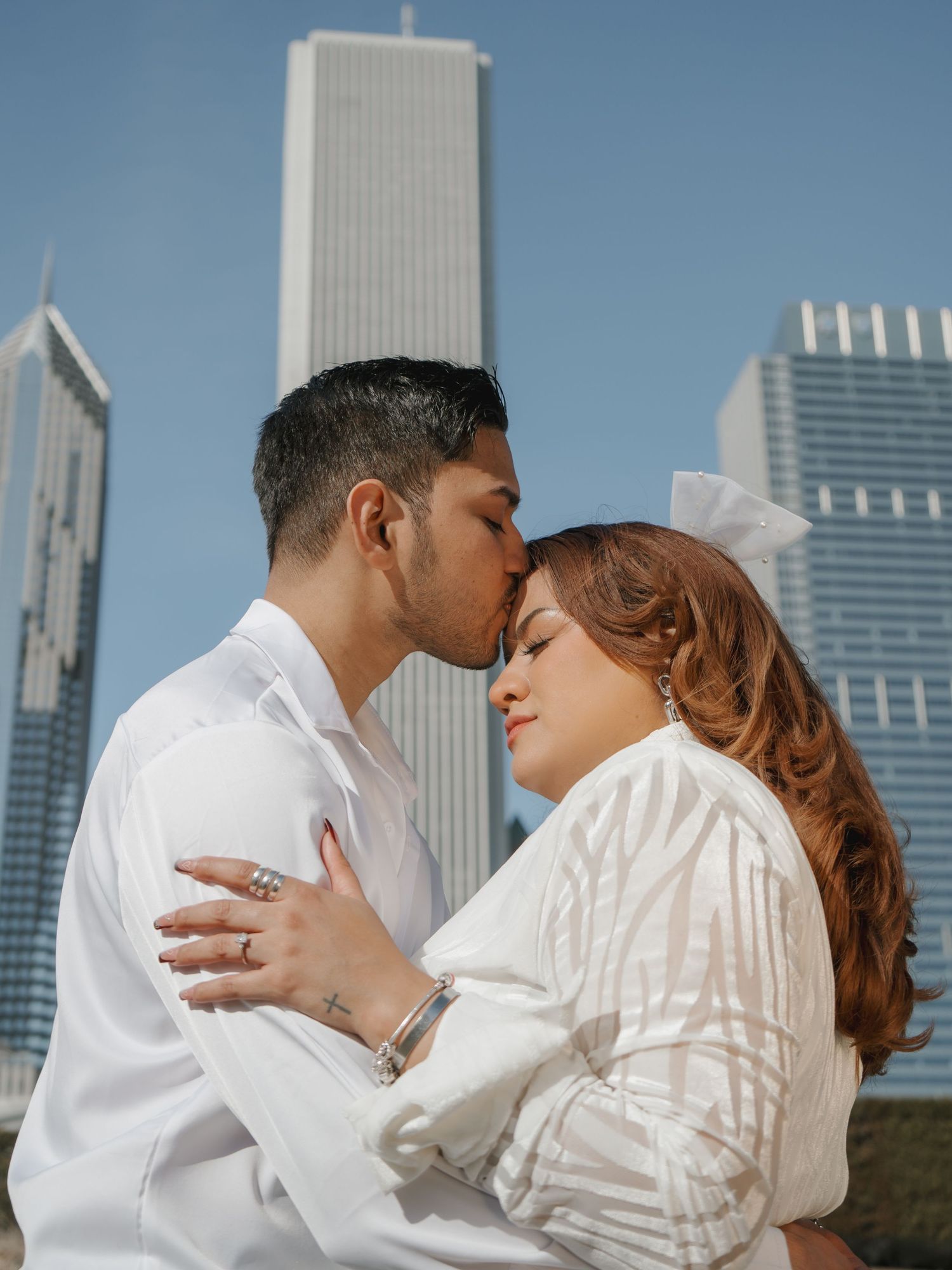 Couple sharing a tender forehead kiss with Chicago skyscrapers in the sunny background.