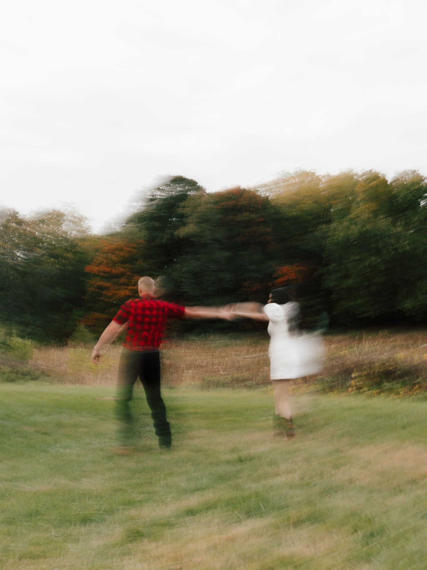 Blurry motion photo of a couple holding hands and spinning in a green field surrounded by autumn trees.