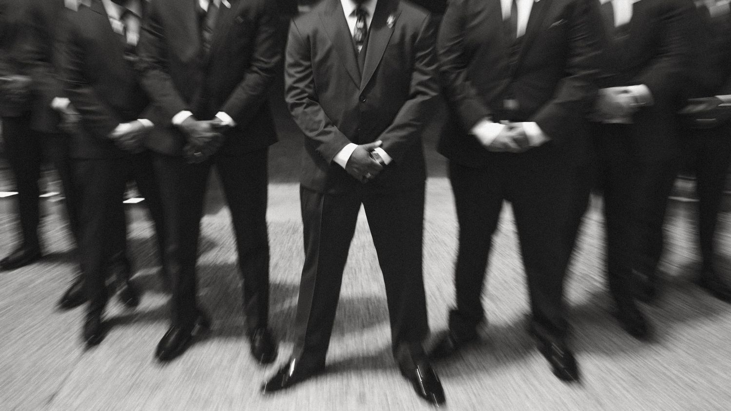 Black and white photo of men in suits standing in a row with motion blur effect.