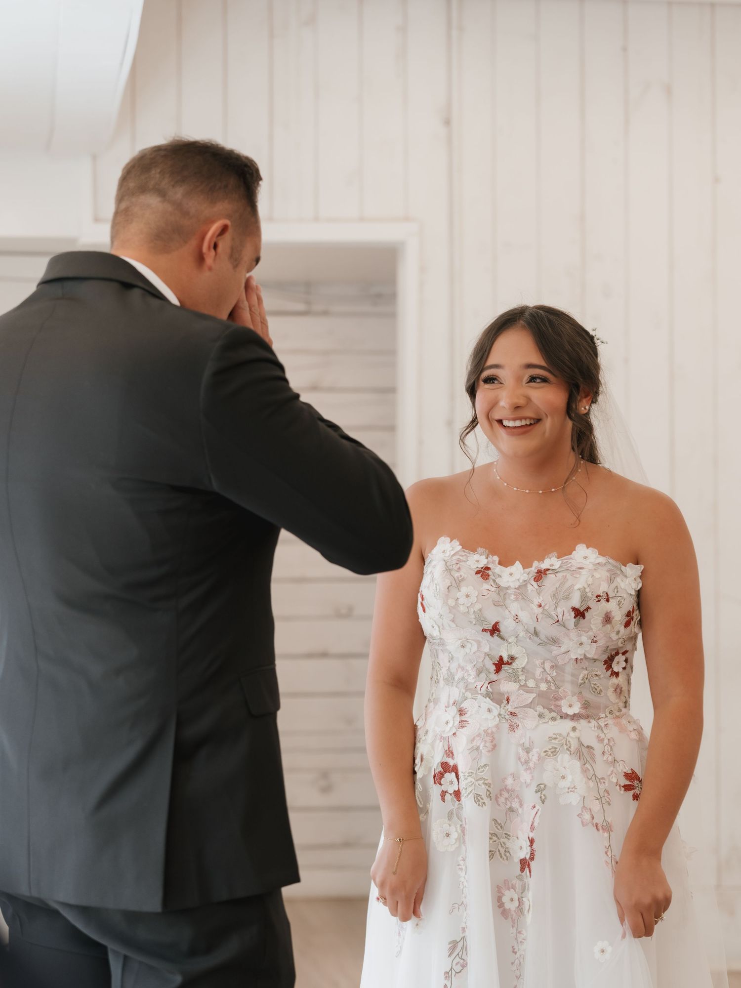 Emotional father of the bride wipes tears as bride in strapless floral wedding dress smiles during first look.
