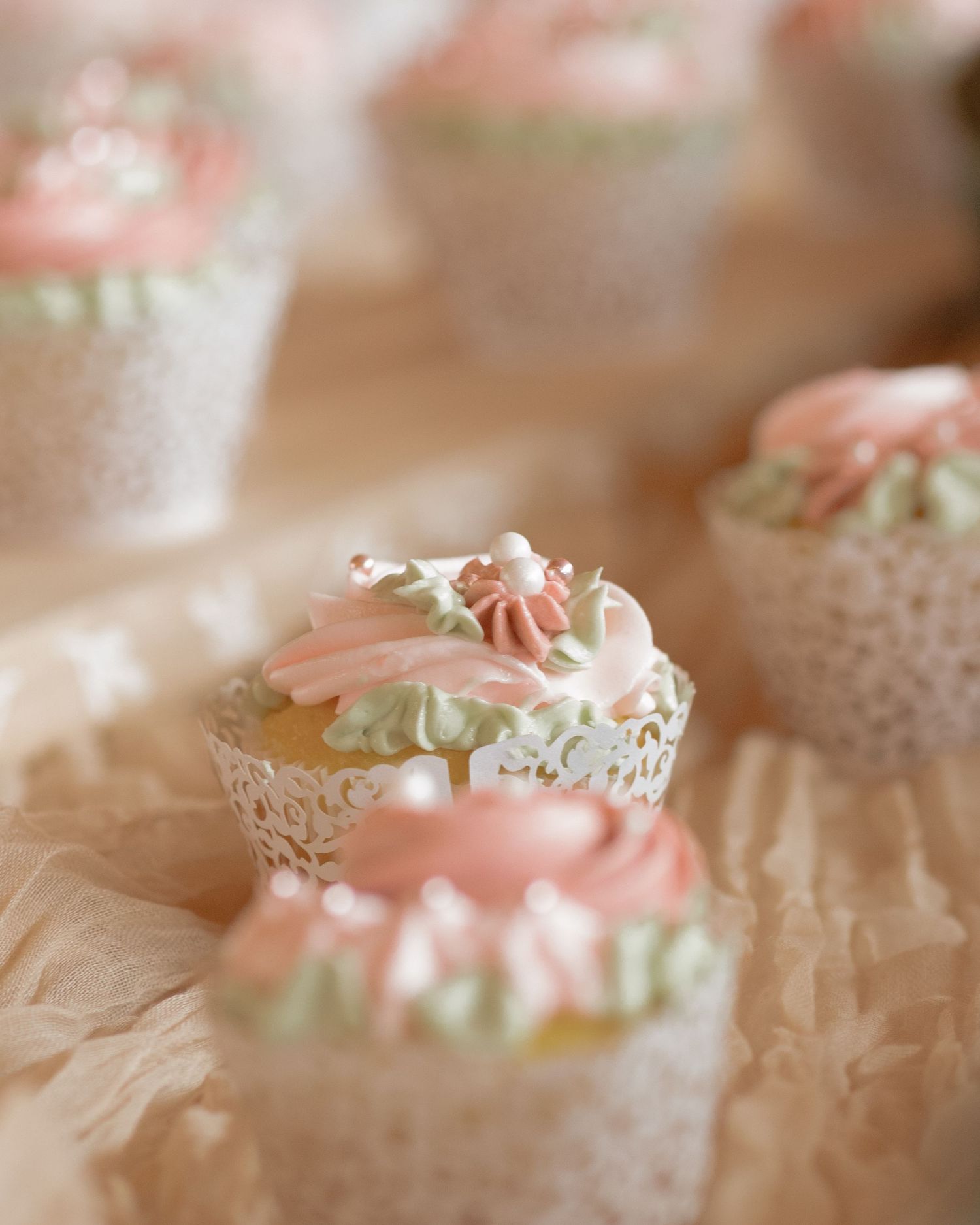 Elegant wedding cupcakes decorated with pink and green frosting flowers in lace cupcake wrappers.