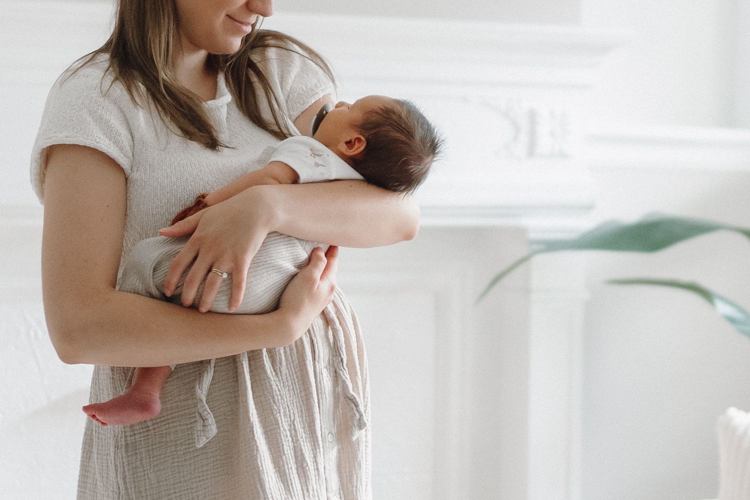 Young mother gently cradling her newborn baby in a bright white living room.