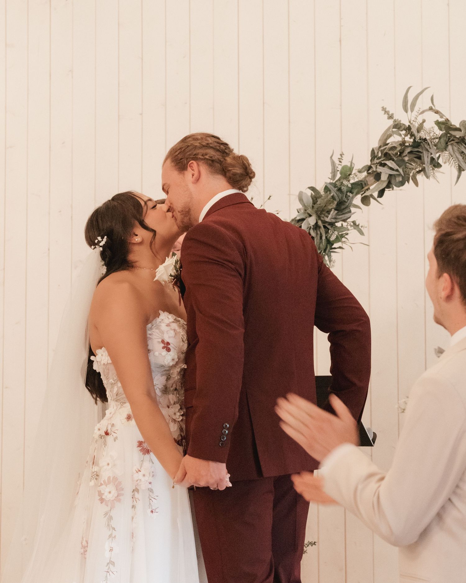 Bride and groom share their first kiss at the altar during an elegant indoor wedding ceremony.