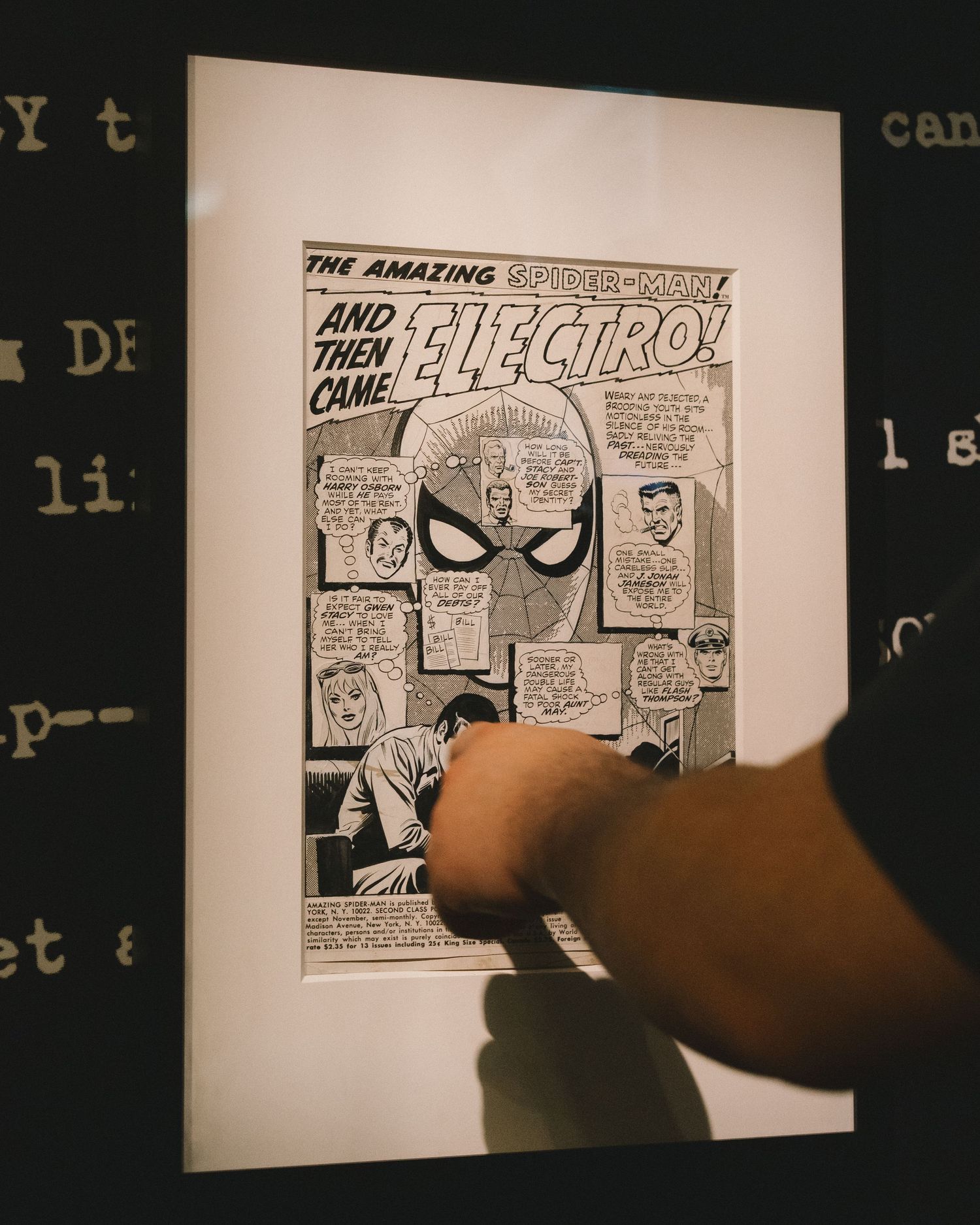 Hand pointing at framed Amazing Spider-Man comic page featuring Electro in black and white at an exhibition.