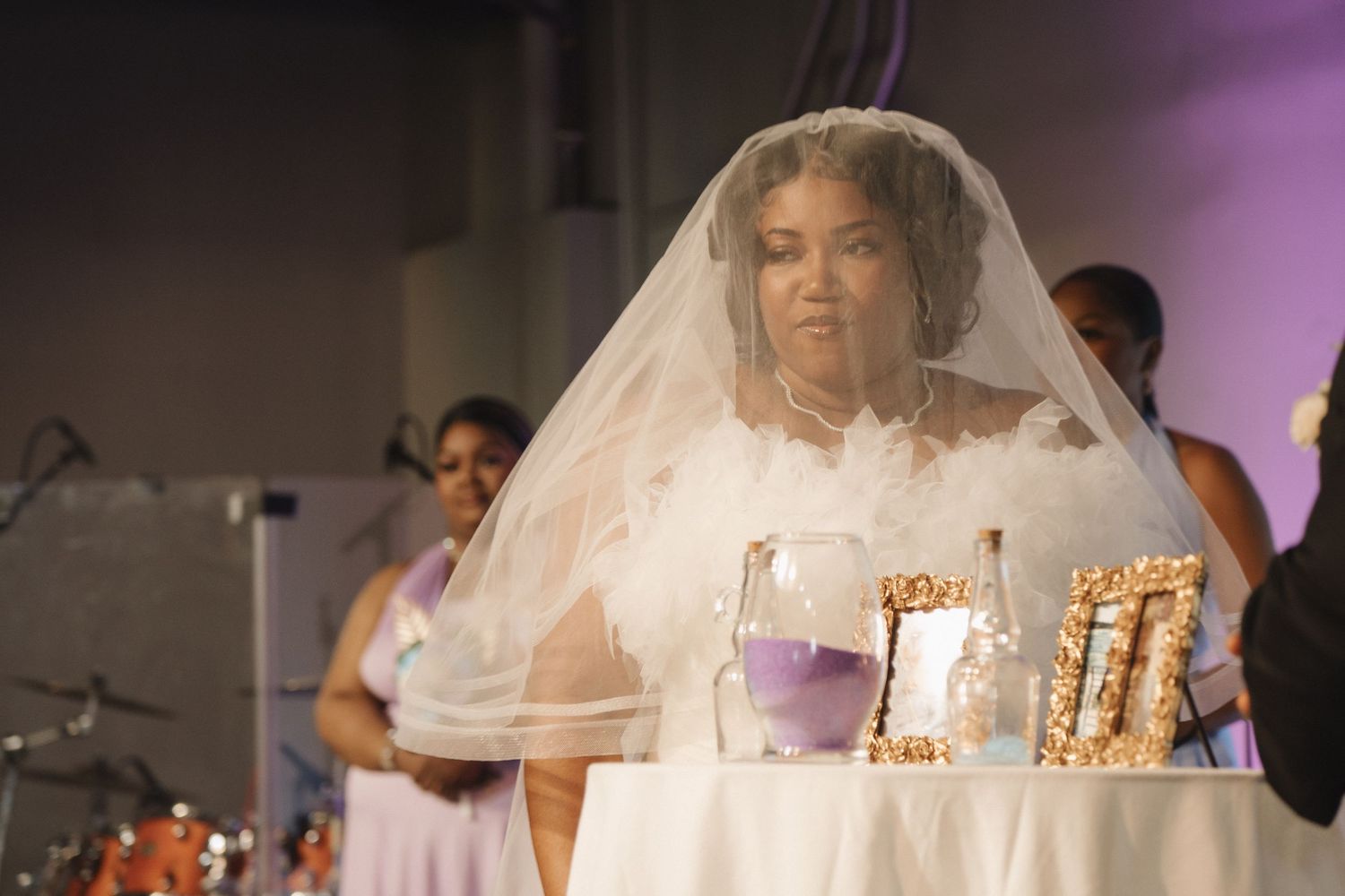 Bride in white wedding gown and veil stands at decorated ceremony table.