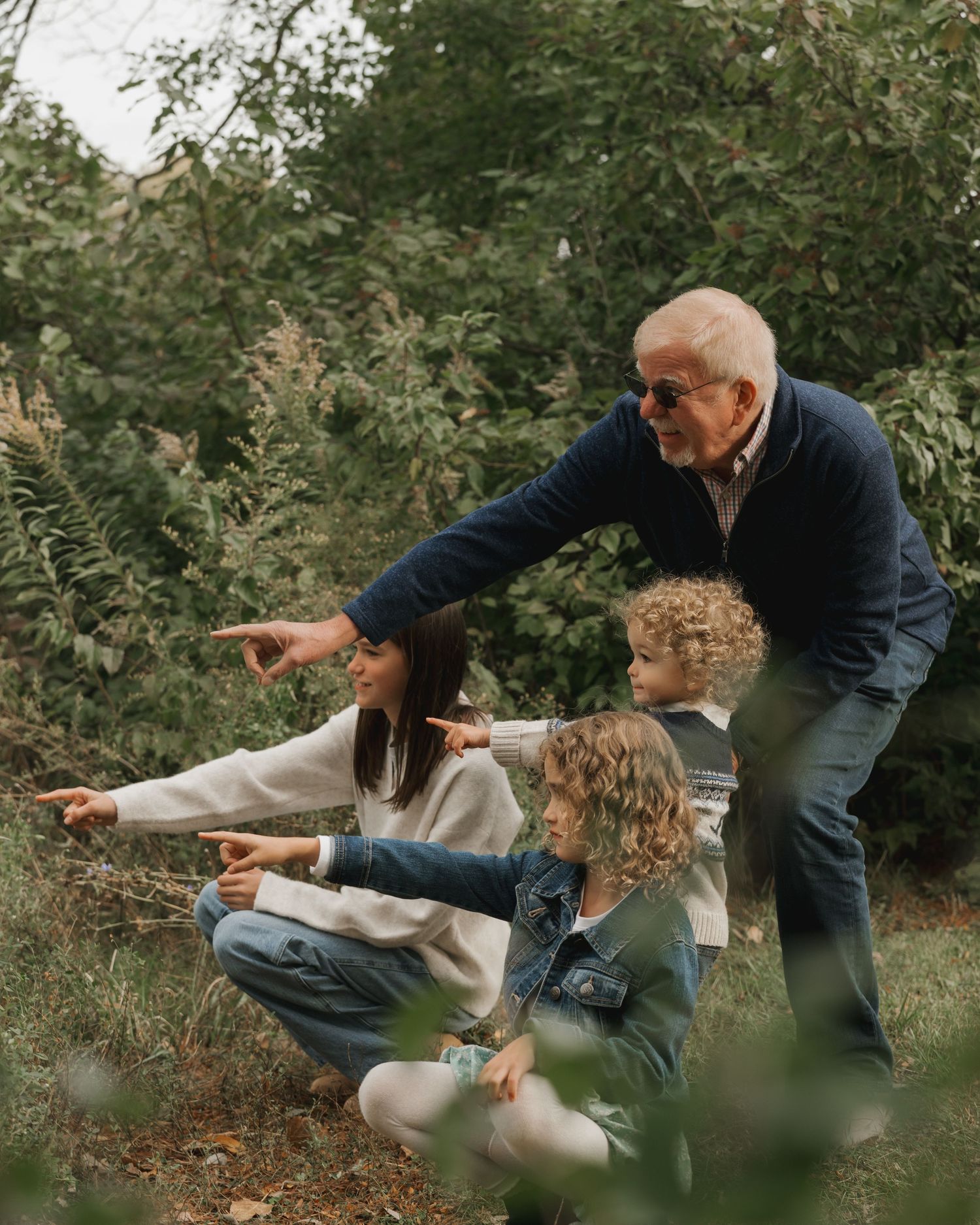 Grandfather pointing into nature with three grandchildren crouching near water.