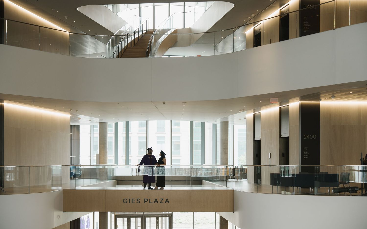 Two people stand on a mezzanine level overlooking Gies Plaza in a modern building atrium, Northwestern University.