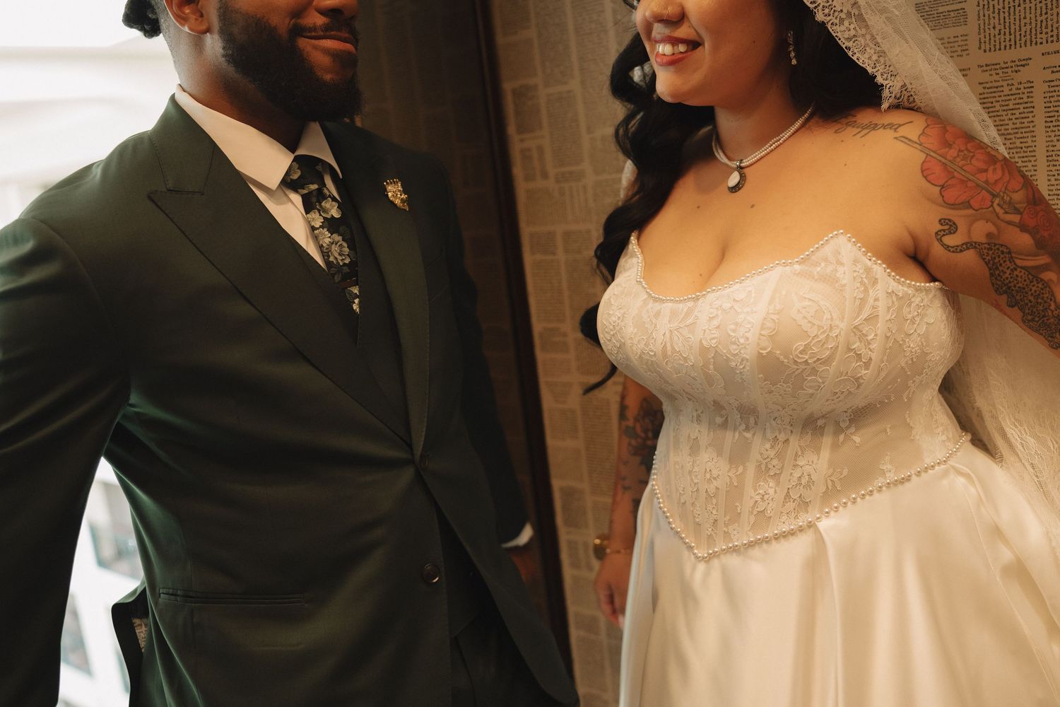 Bride in lace strapless gown with tattoos and groom in dark suit share a joyful wedding moment.