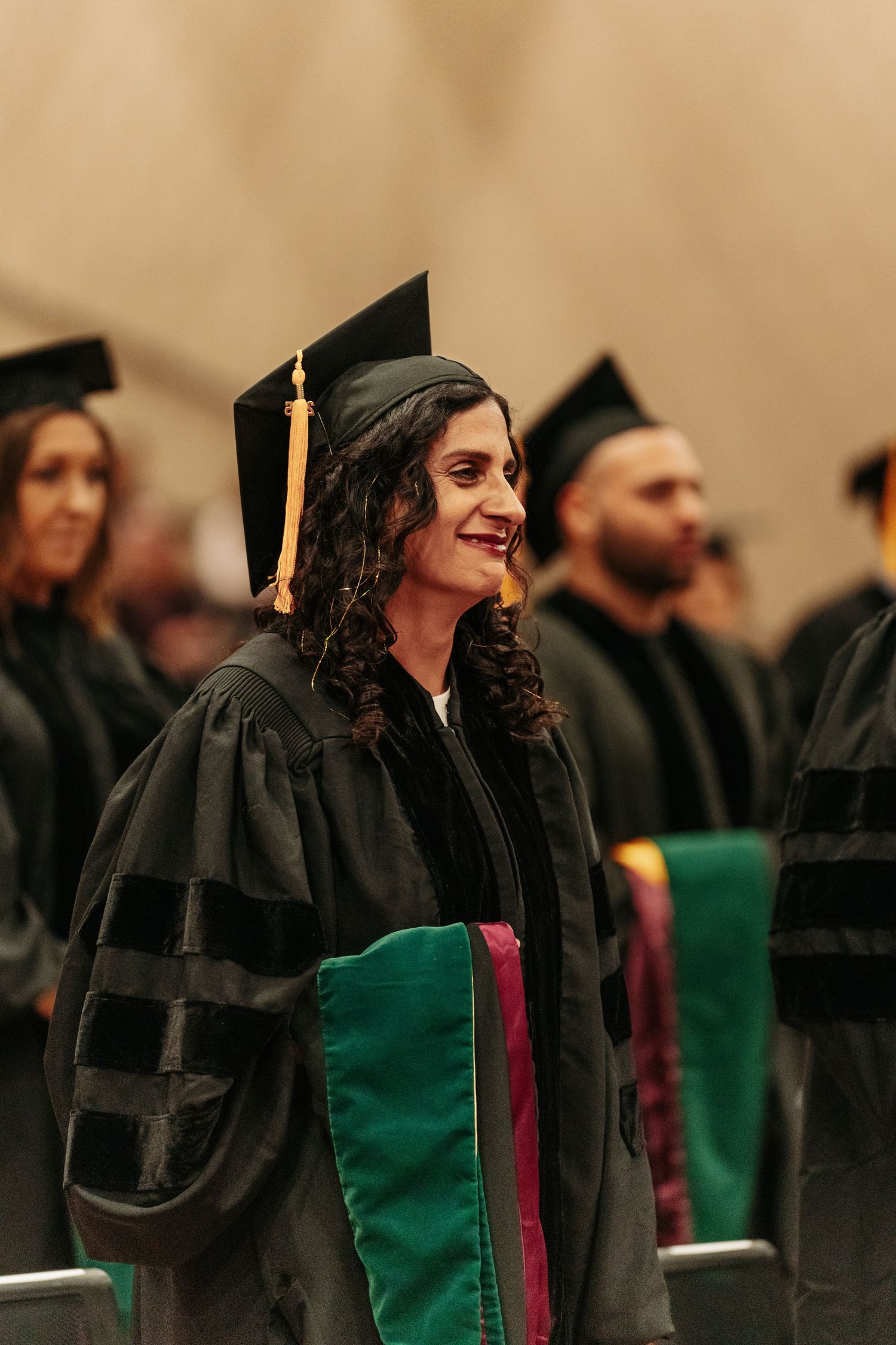 Smiling woman in doctoral graduation cap and gown stands among fellow graduates at a commencement ceremony.