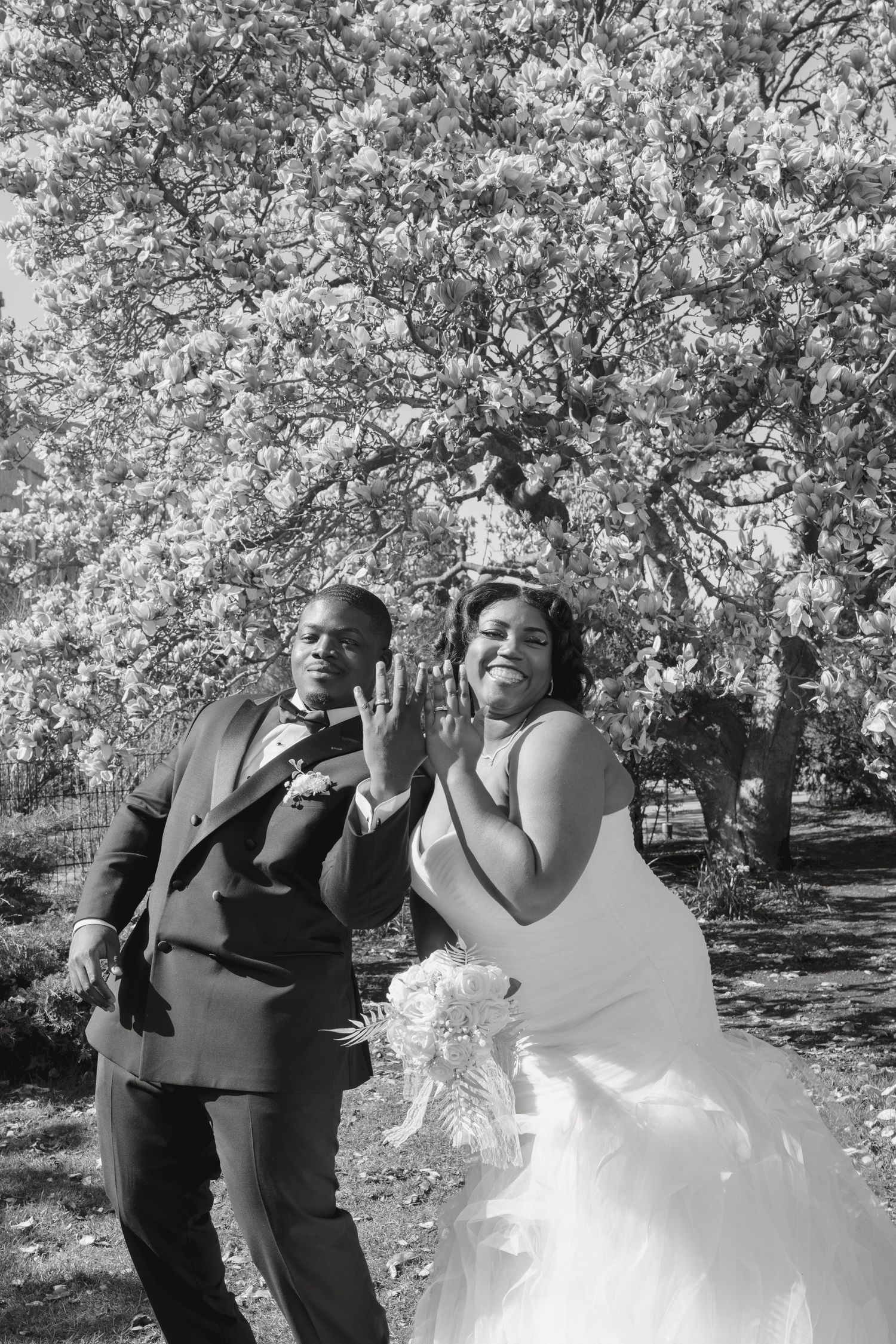 Glowing with happiness, a bride and groom pose playfully, showcasing their wedding bands against a backdrop of ethereal floral textures.
