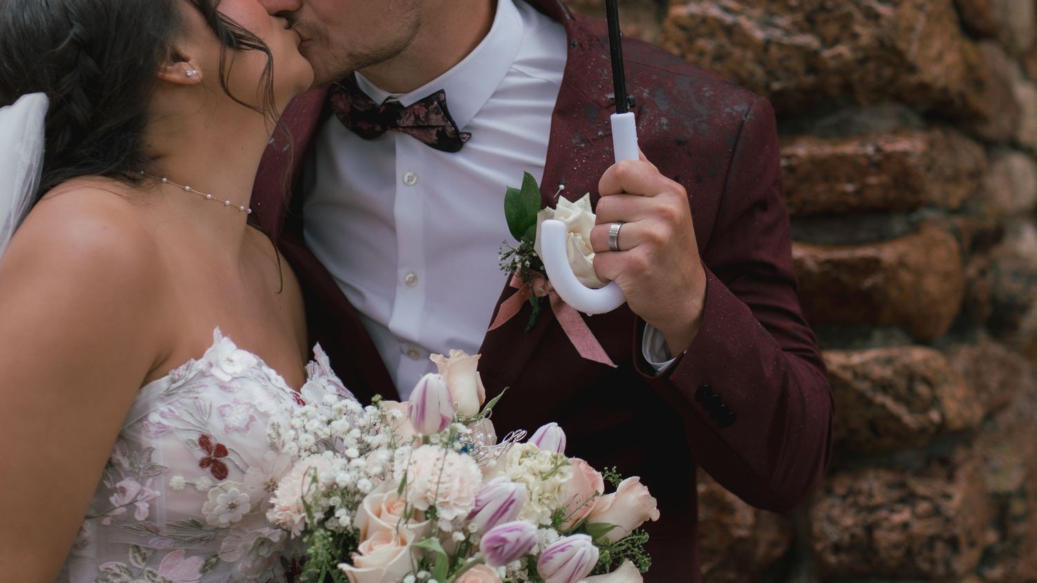 A bride and groom share a kiss on their wedding day, with the groom holding a white boutonniere.