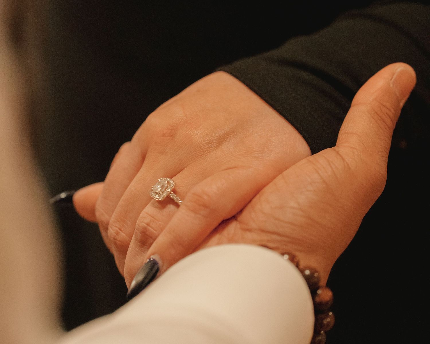 Close-up of a cushion cut diamond engagement ring on womans hand held by partner.