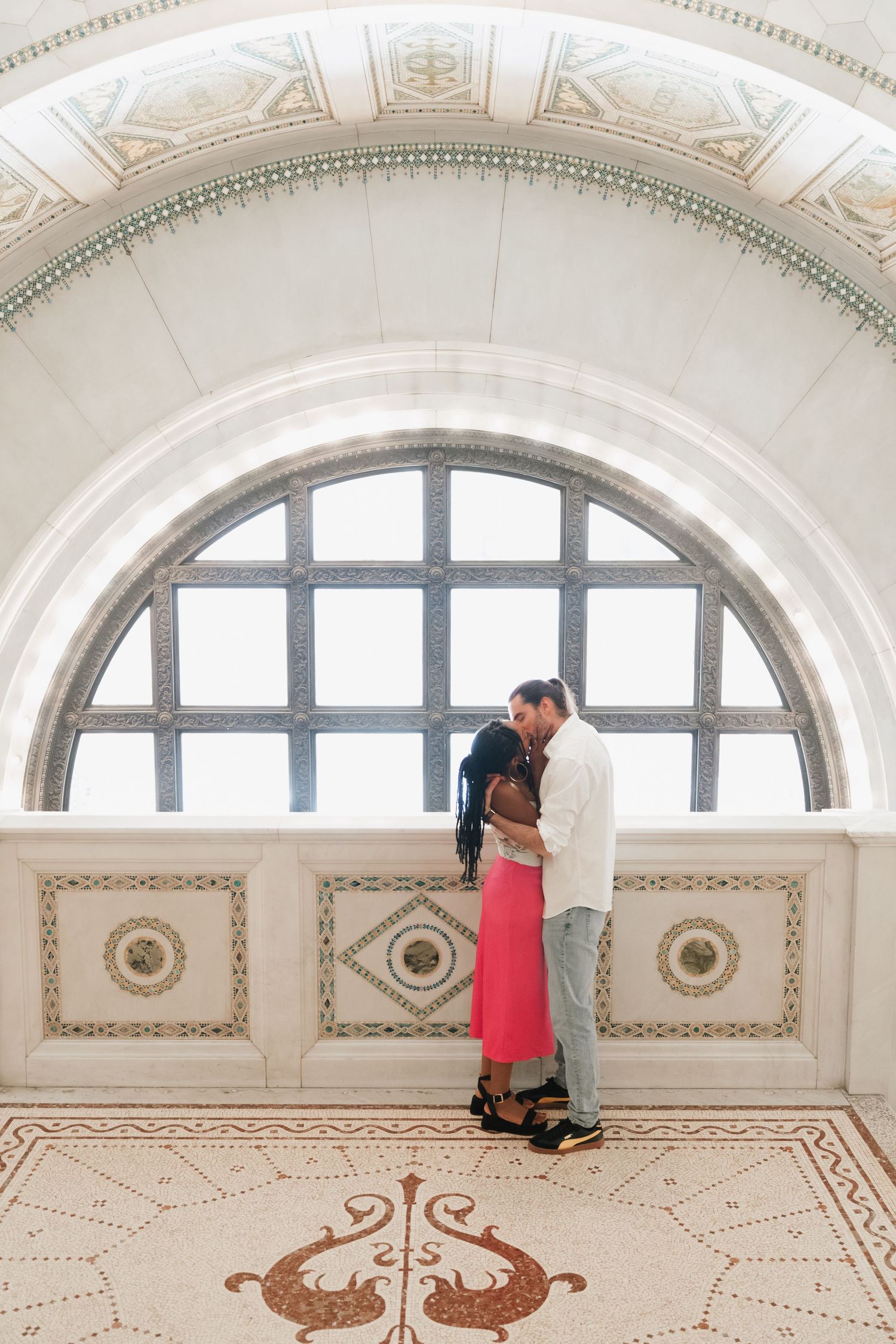 Couple sharing a romantic kiss under ornate arched window in a grand historic building in Chicago, IL.