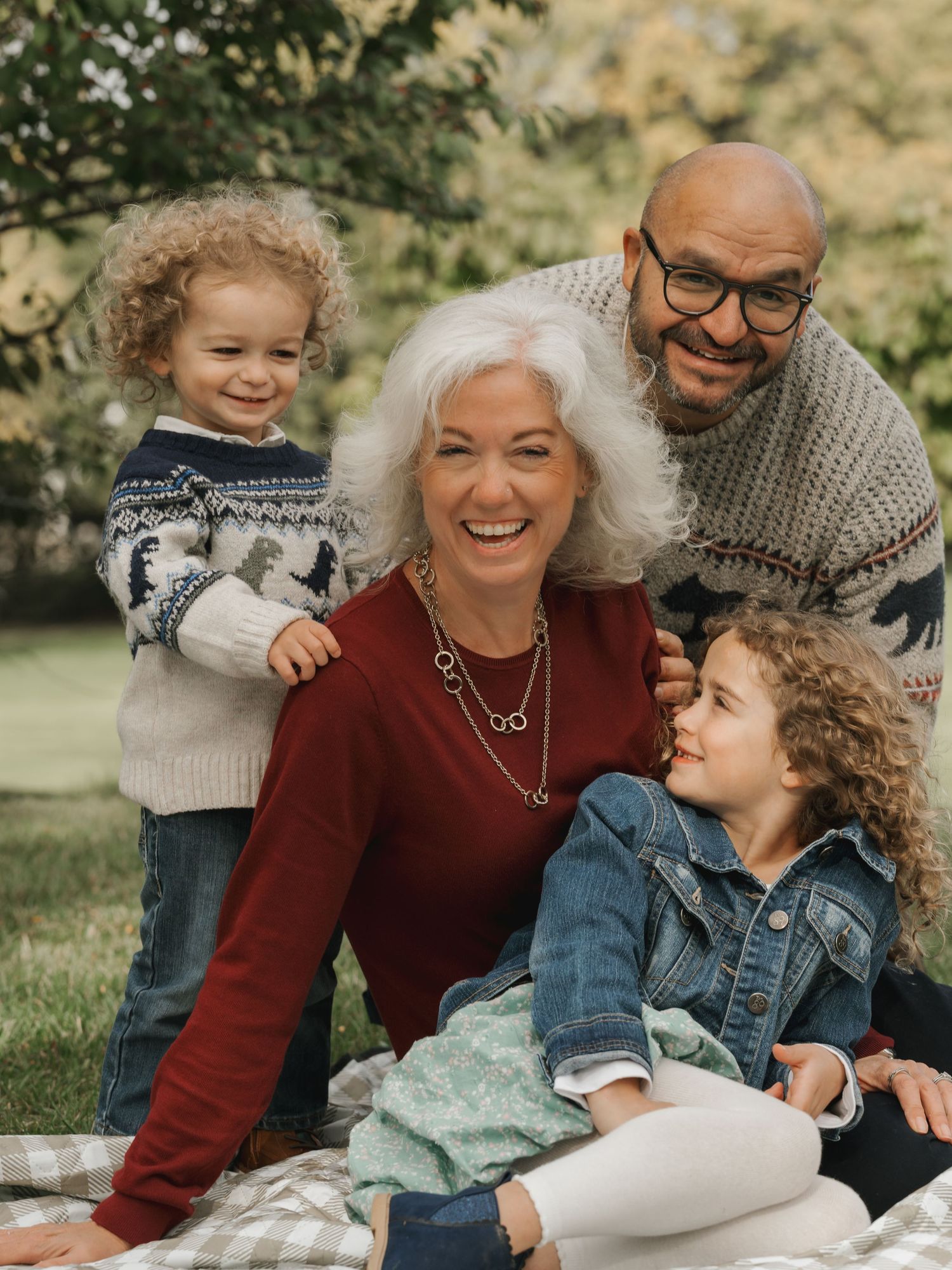 Parents laugh with two curly-haired children during an outdoor family picnic.