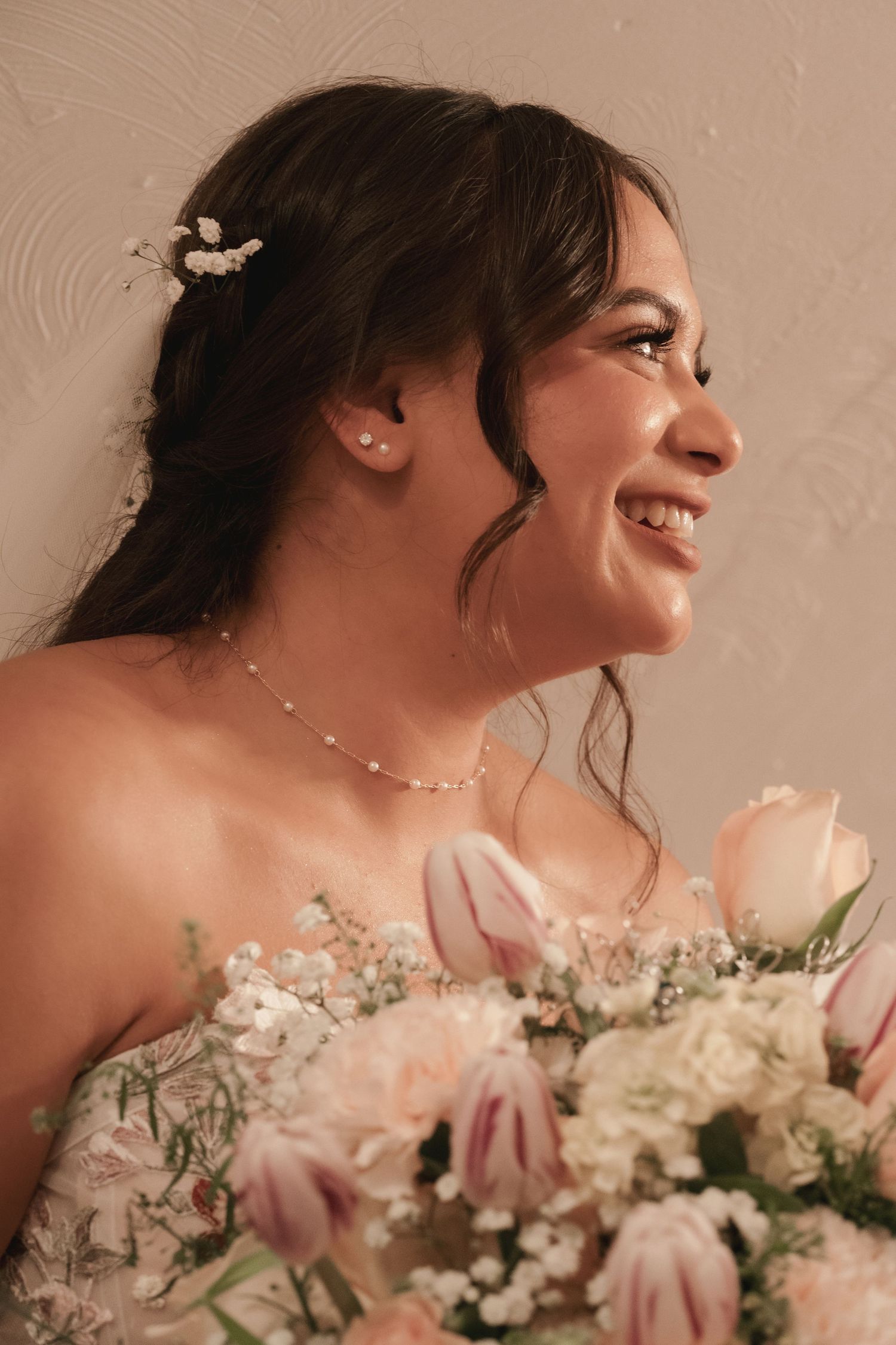 Radiant bride smiles holding a bouquet of pink tulips and white flowers on her wedding day.