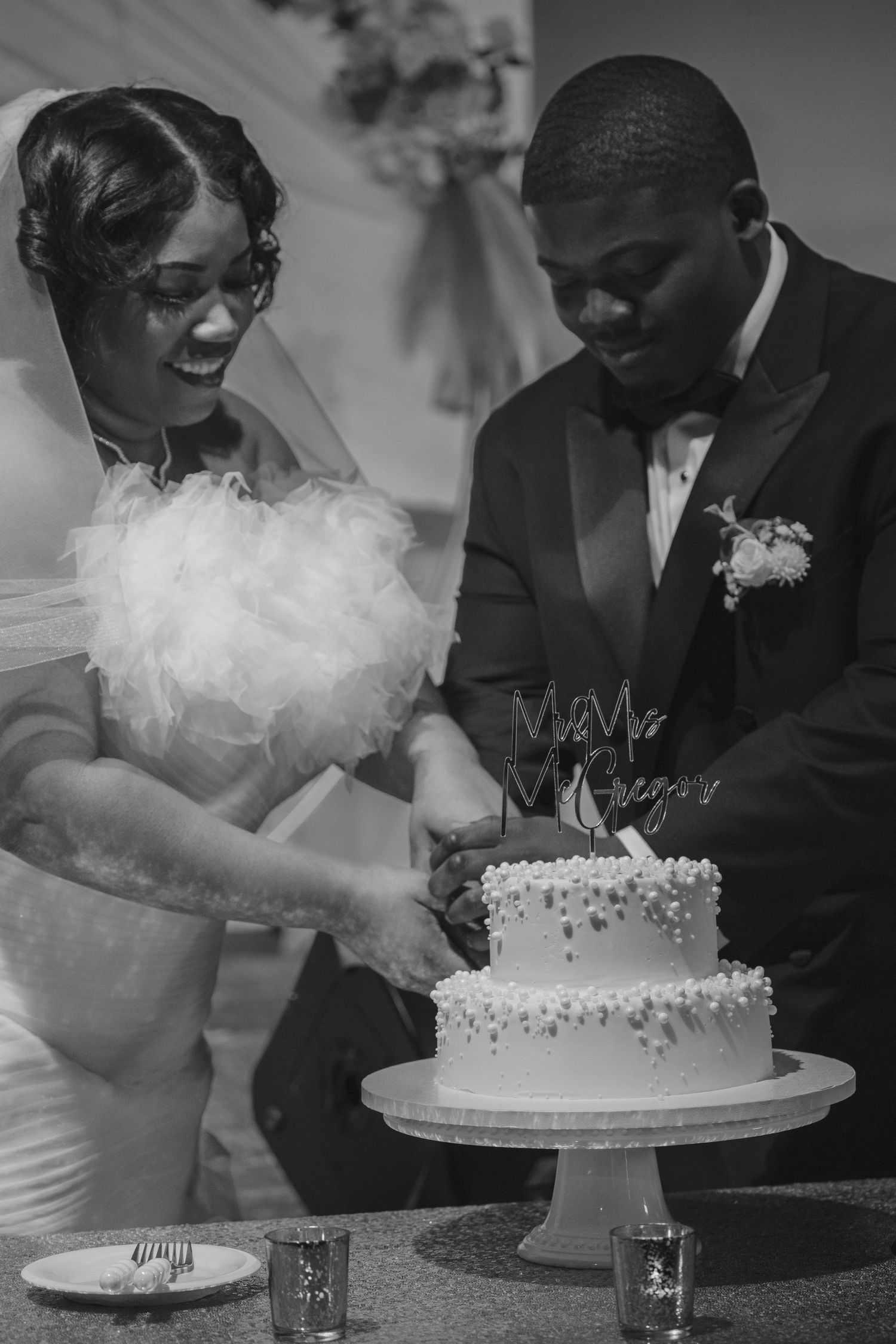 Black and white photo of a bride and groom cutting their wedding cake together at their reception.