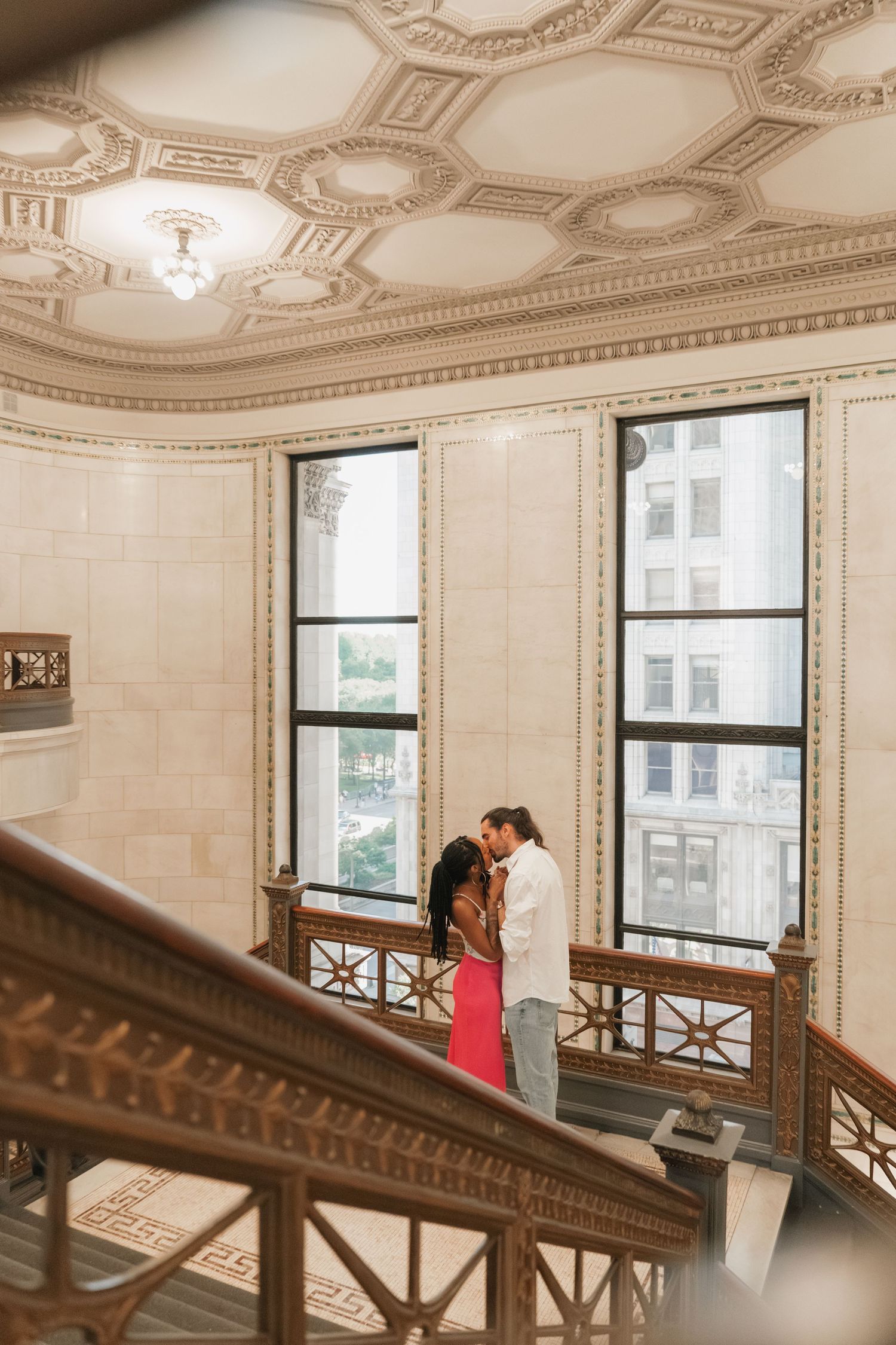 Couple kissing on a balcony inside a stunning ornate building with coffered ceiling.