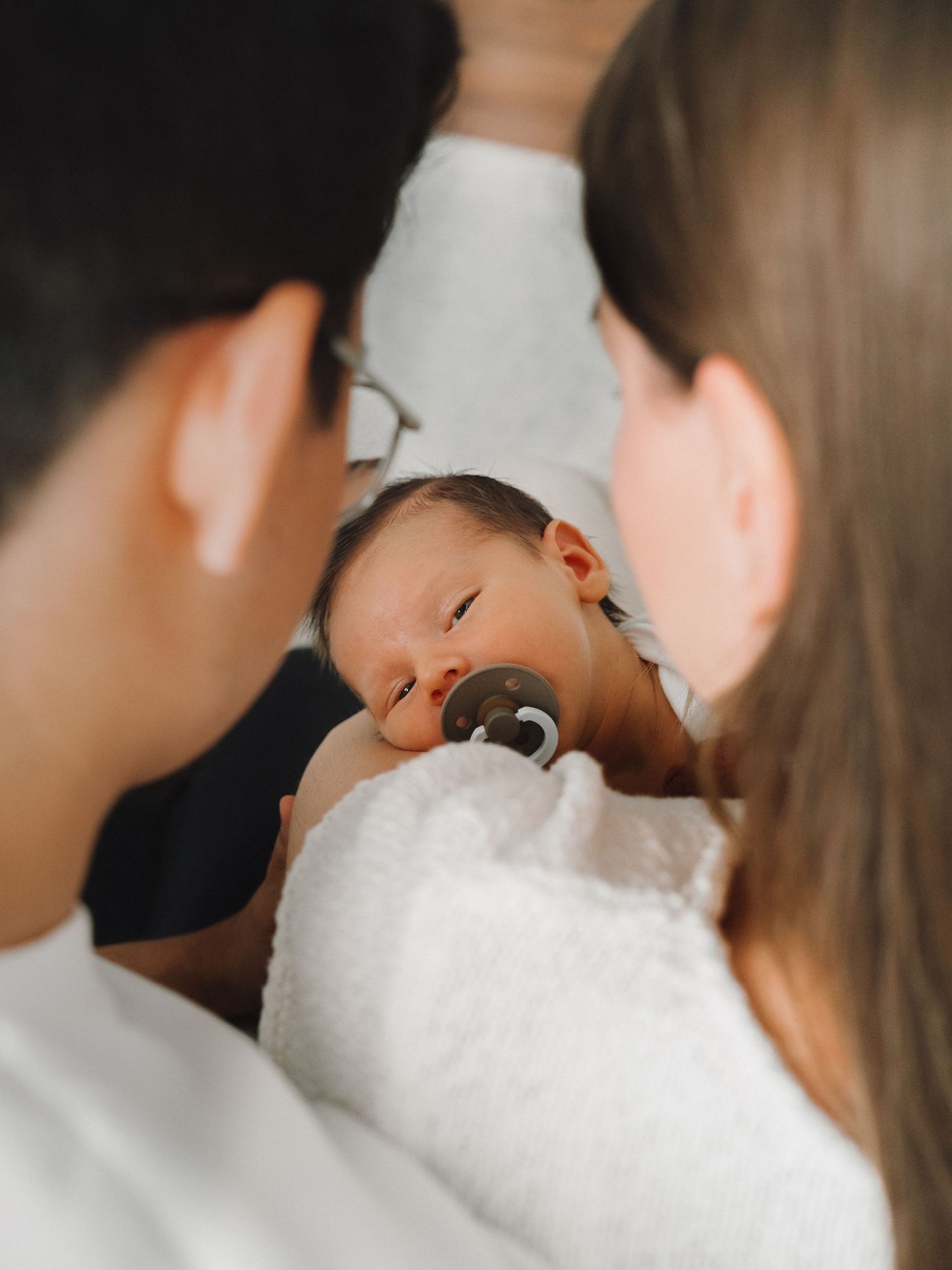 New parents cradling their sleepy newborn baby with pacifier.