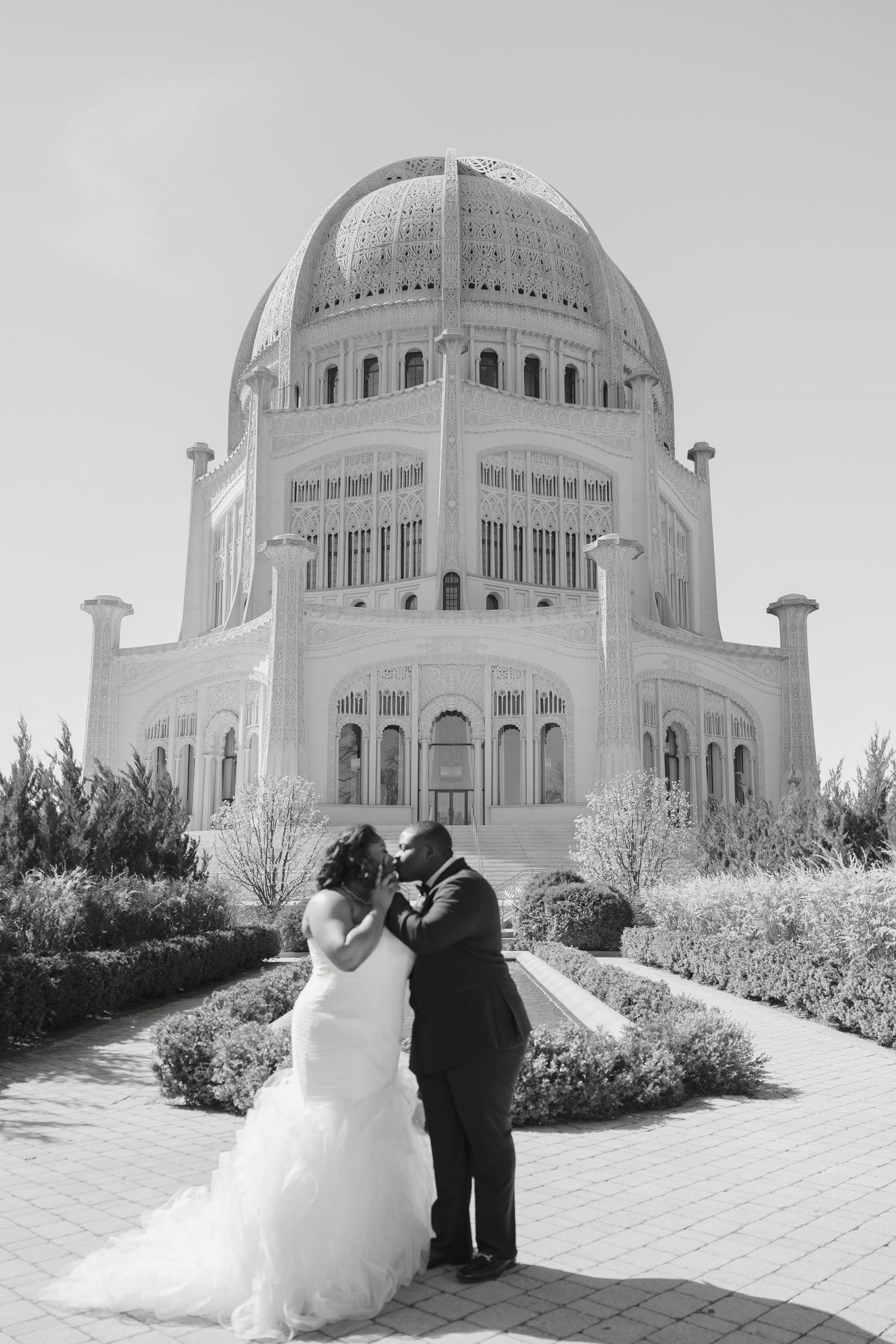 Black and white photo of a couple kissing in wedding attire in front of the Bahai Temple in Wilmette, Illinois.
