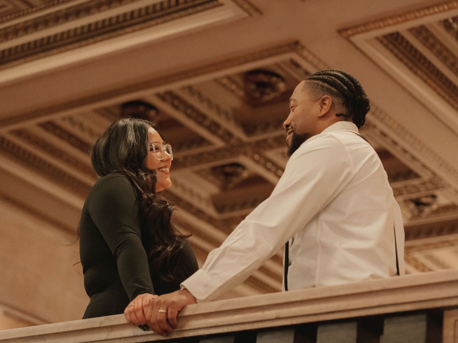 Couple sharing a romantic conversation on a balcony with ornate ceiling above.