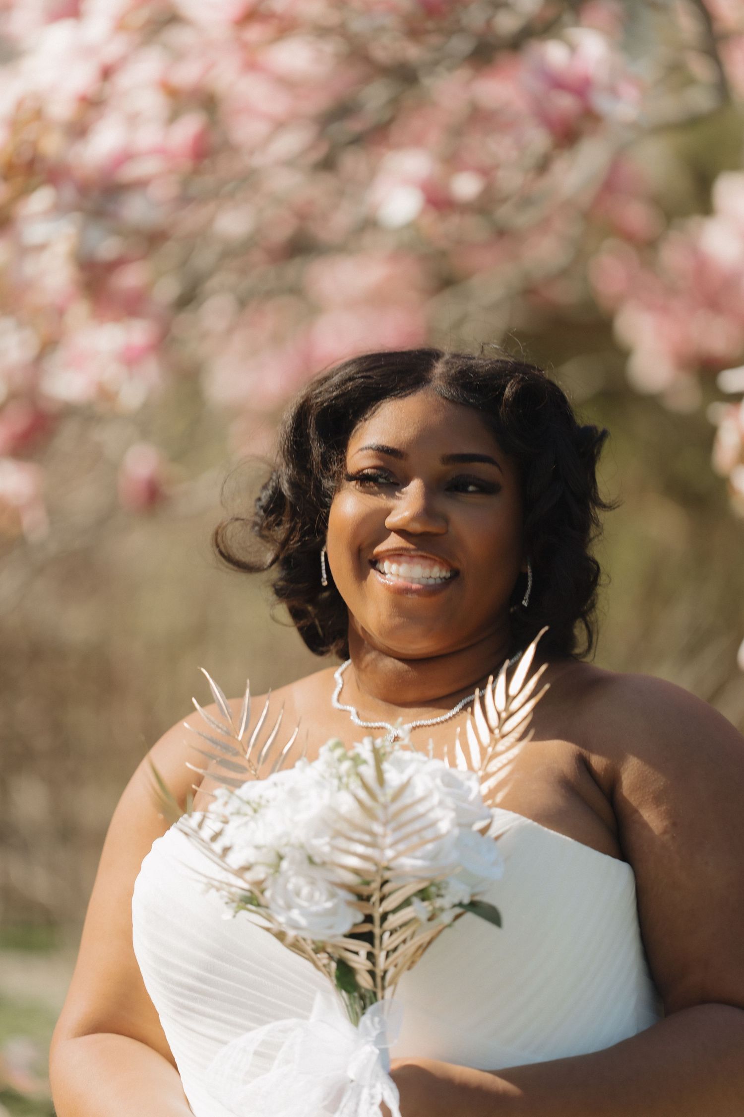 Close-up bridal portrait featuring a strapless wedding dress and a unique white floral bouquet with gold leaf accents.