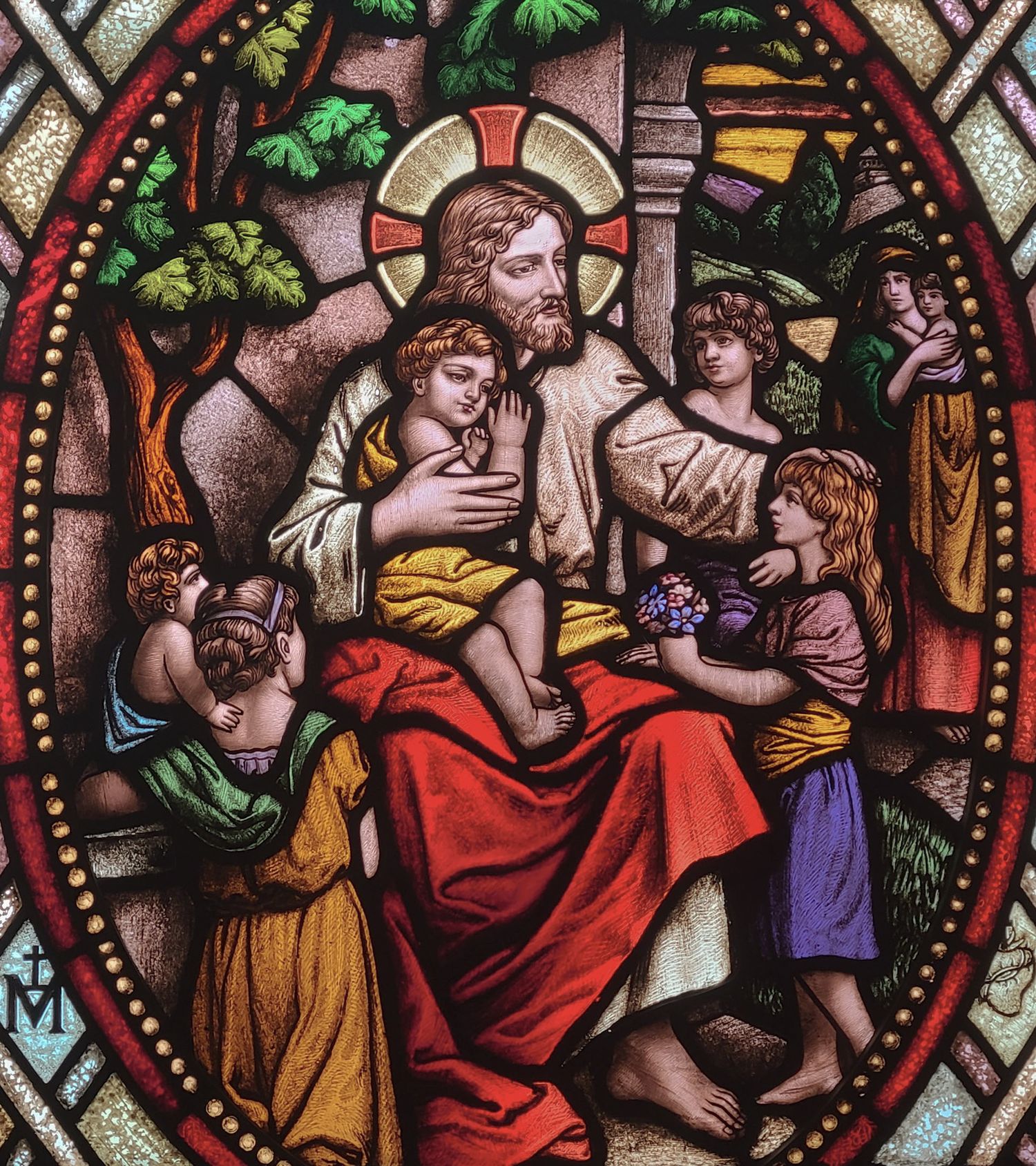 Stained glass window depicting Jesus Christ surrounded by children, rendered in vibrant red, gold, and blue hues.