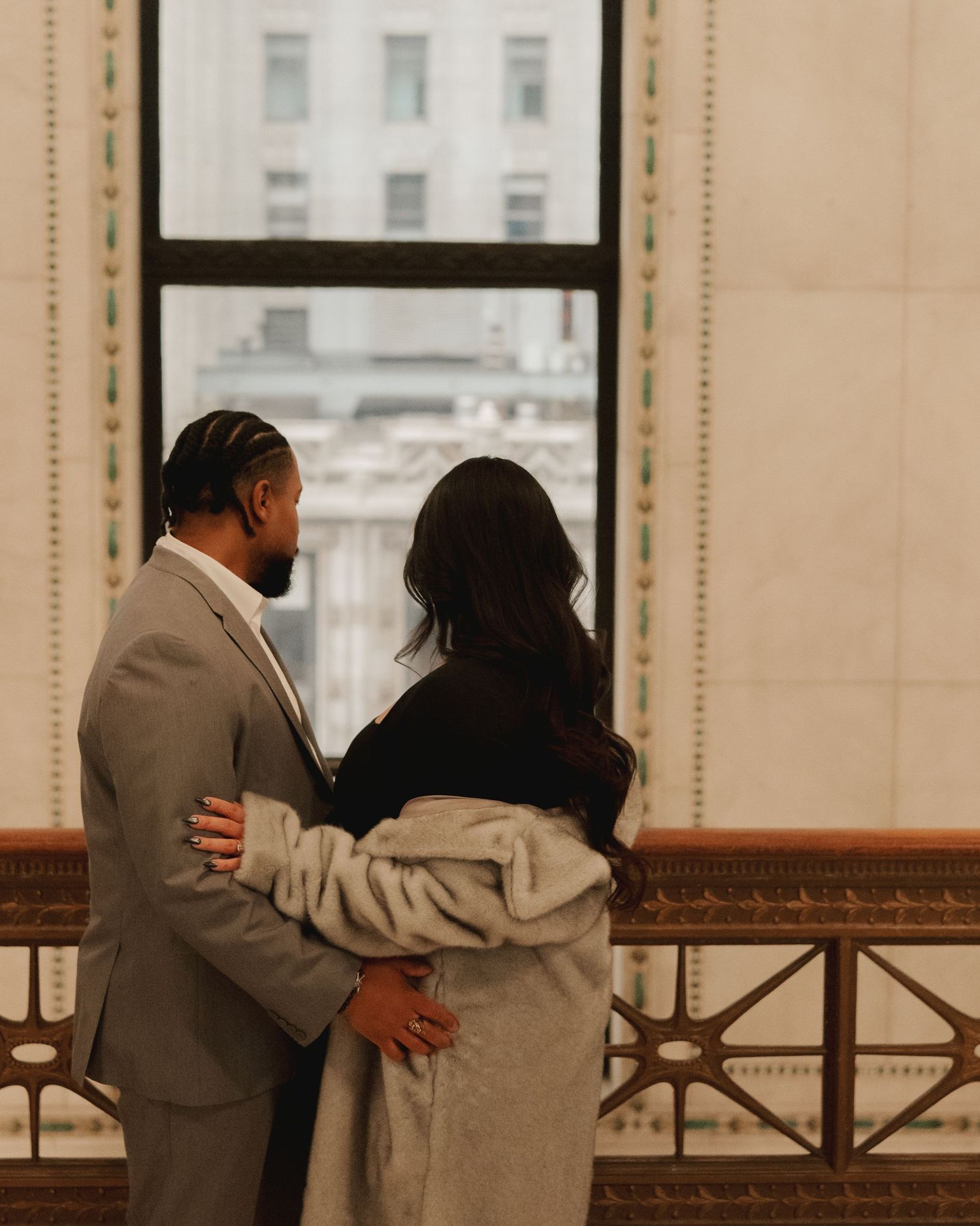 Couple embracing while gazing out large window at city buildings together.