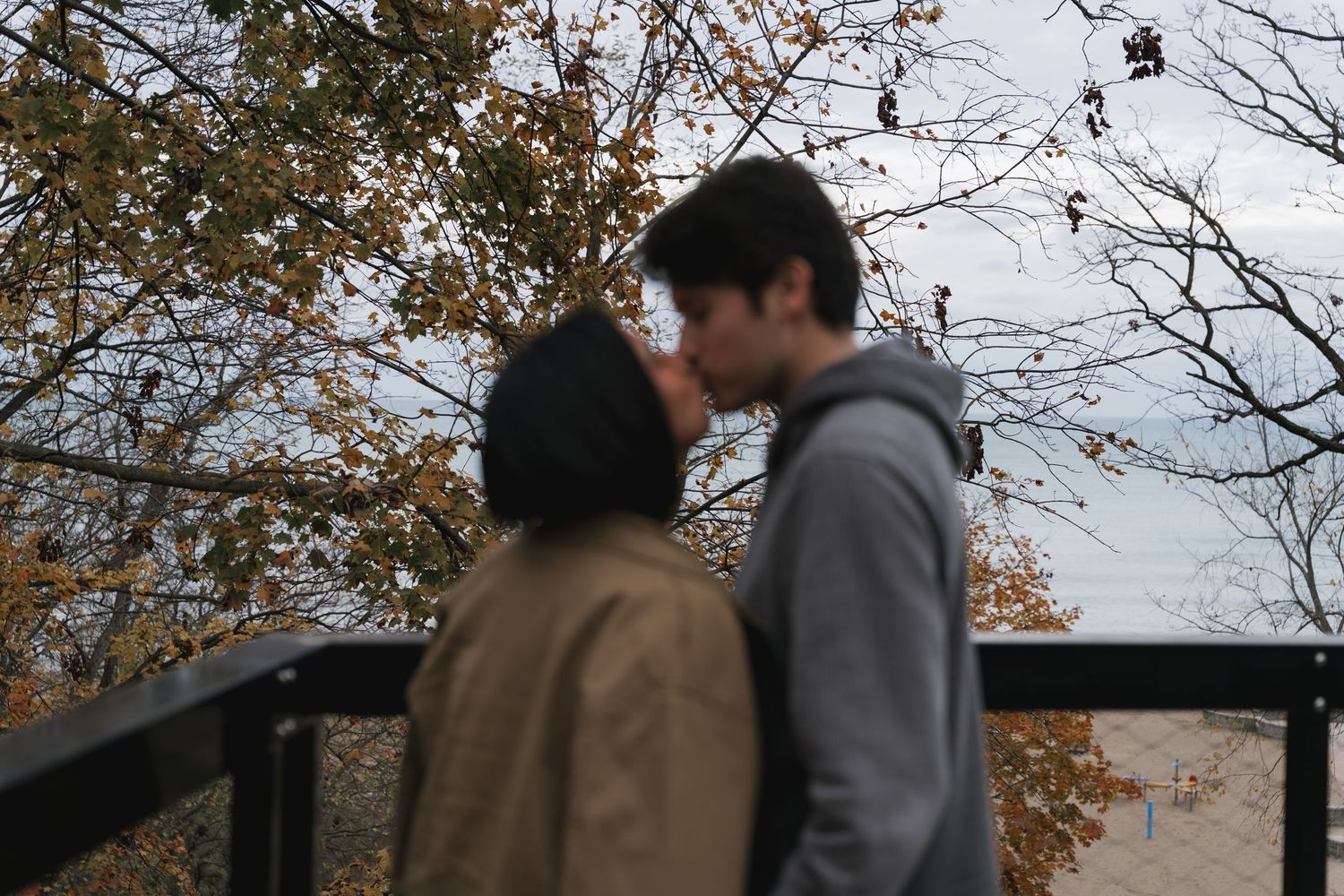 A couple shares a romantic kiss on a bridge surrounded by autumn foliage.