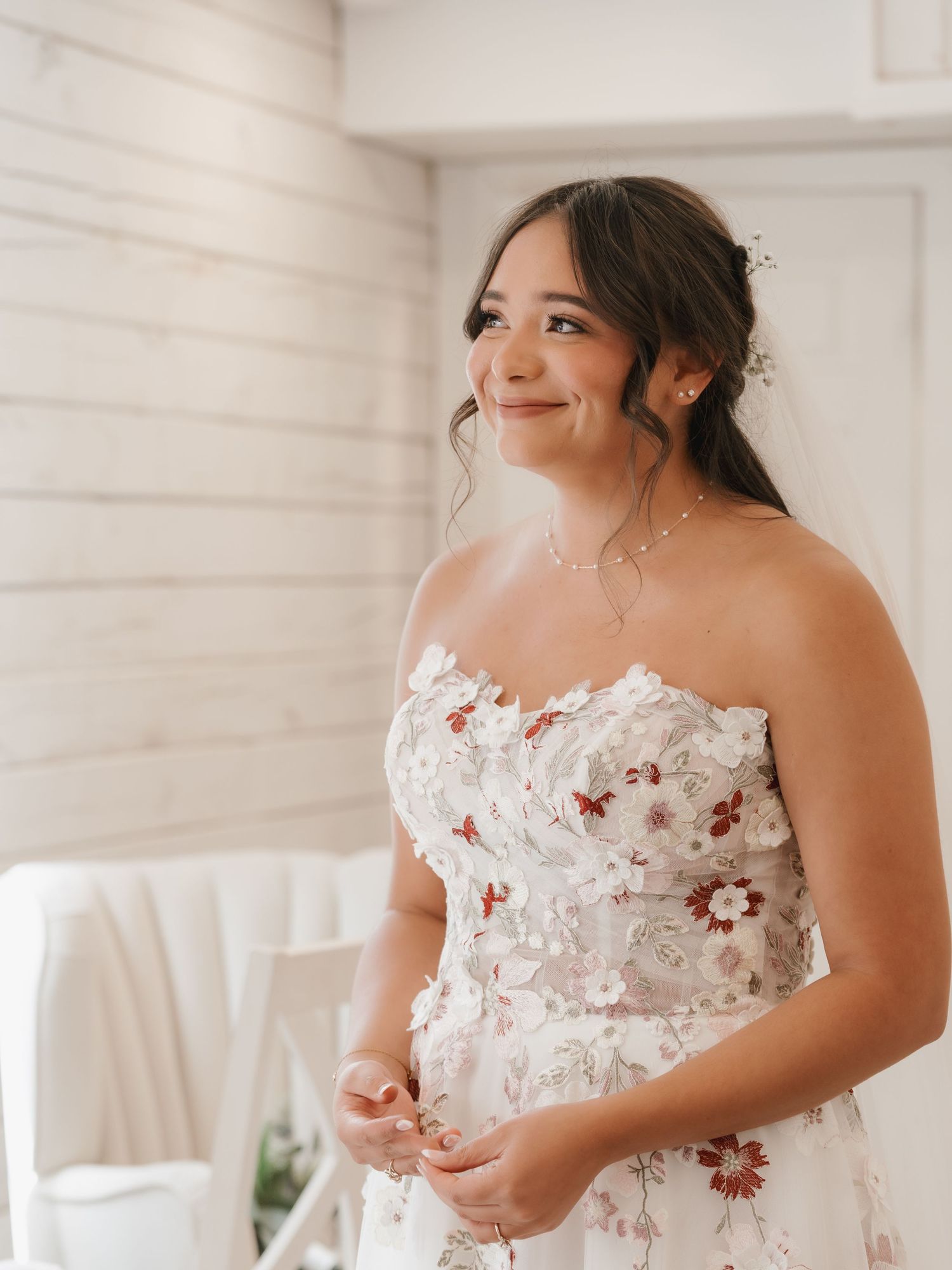 Smiling bride in a strapless floral applique wedding gown standing in a bright white room.