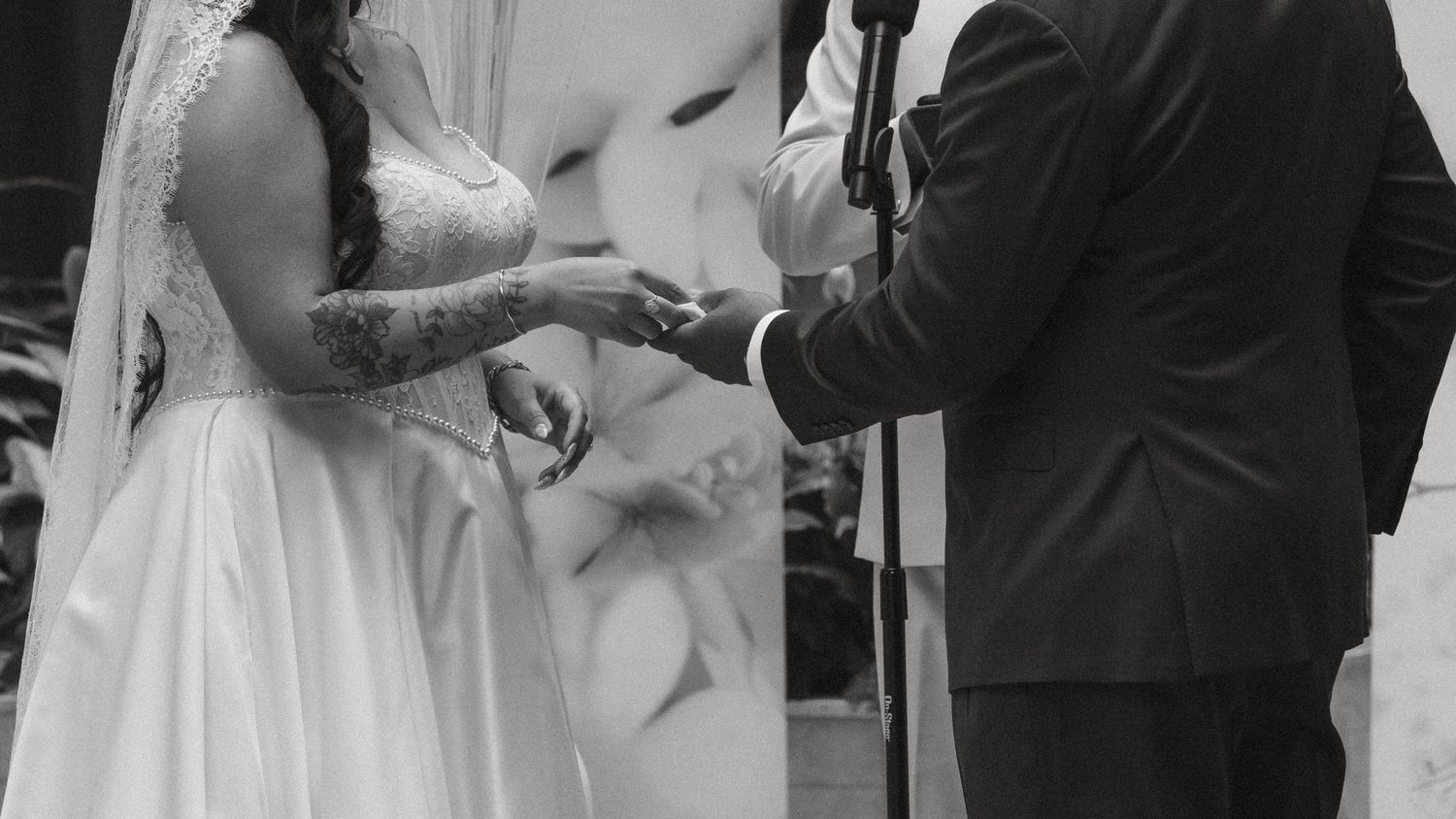 Black and white wedding photo of bride placing ring on groom's finger at altar ceremony.