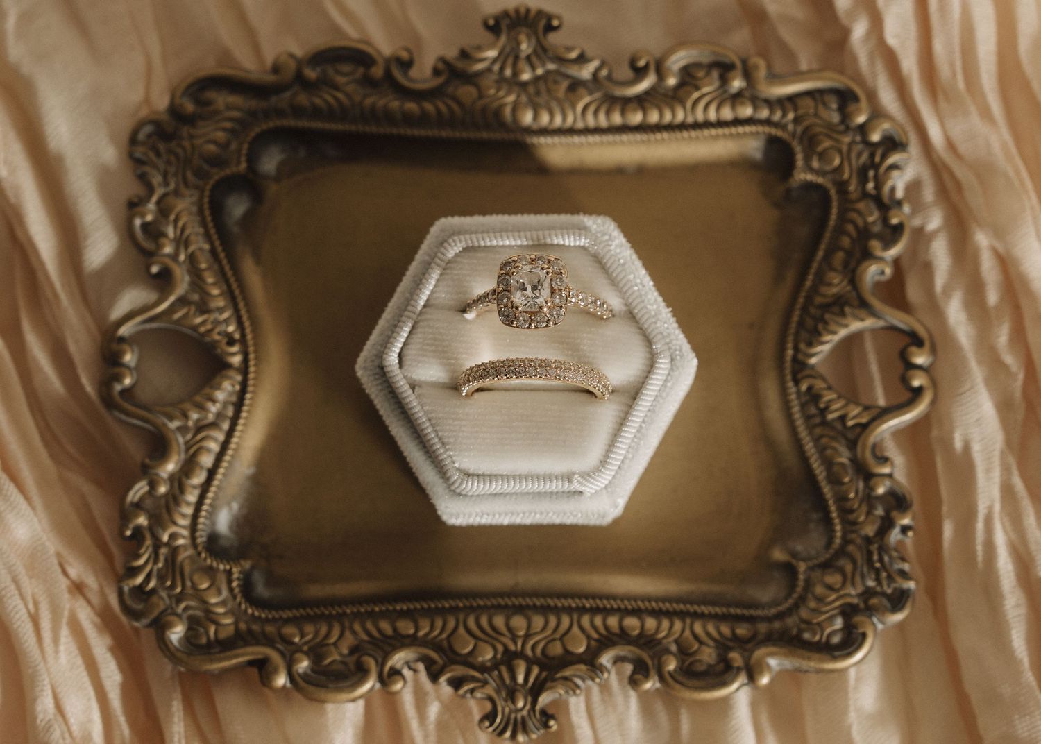 Gold halo engagement ring displayed in a white hexagon ring box on an ornate vintage gold decorative tray.