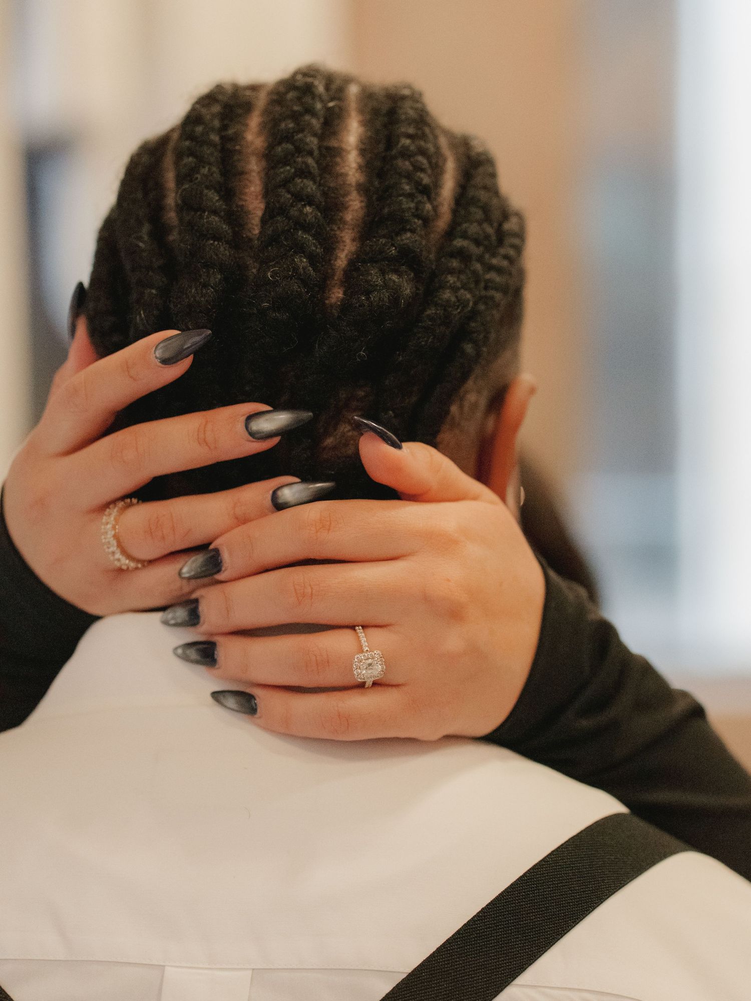 Close-up of hands with engagement ring embracing mans head with braided hair.