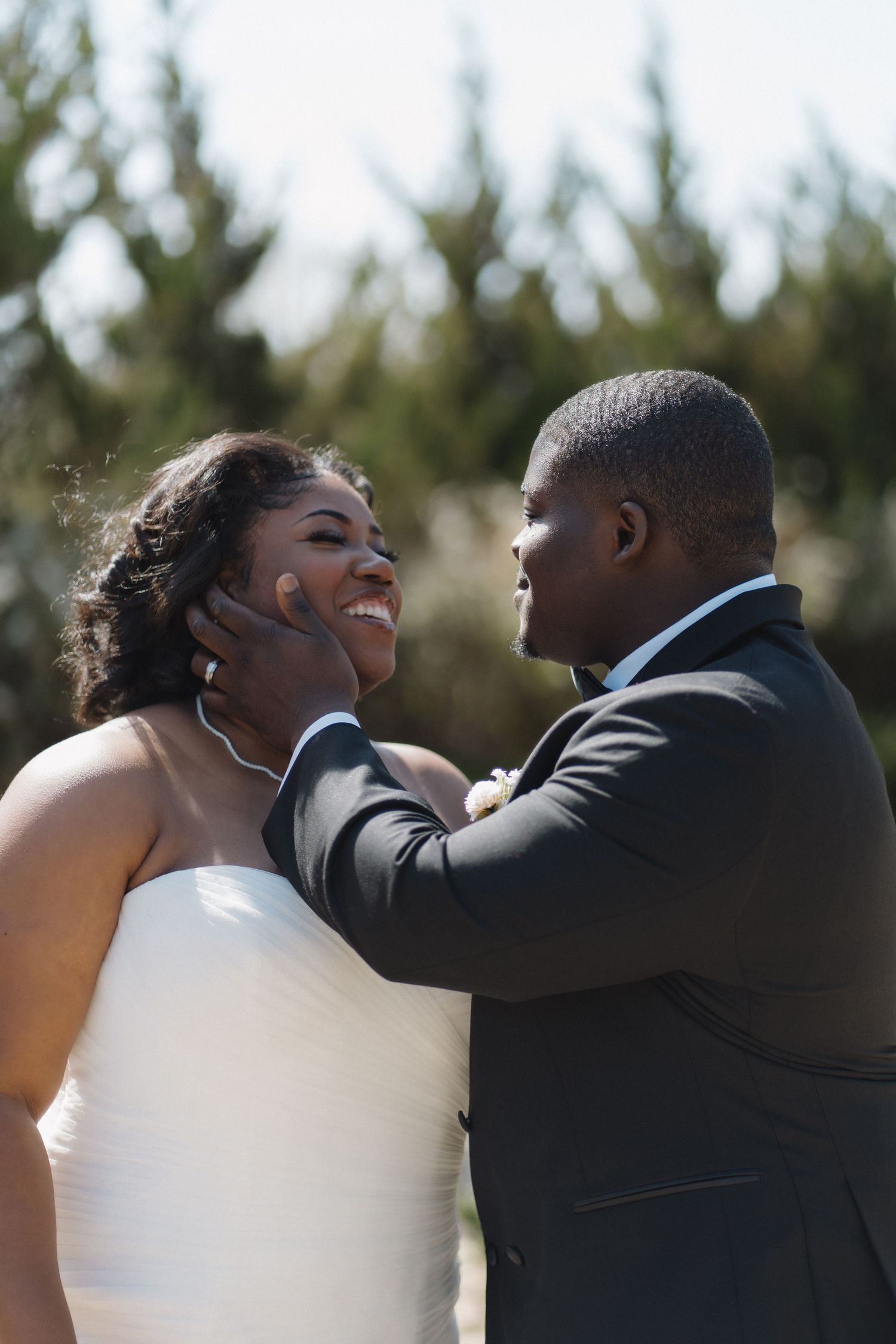 A bride and groom share a tender moment outdoors, while the groom is caressing his new bride.