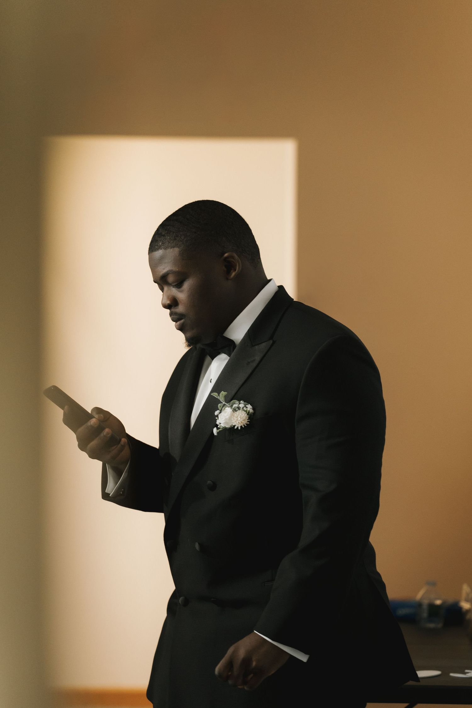 Groom in black tuxedo with boutonniere reads a note before his wedding ceremony.