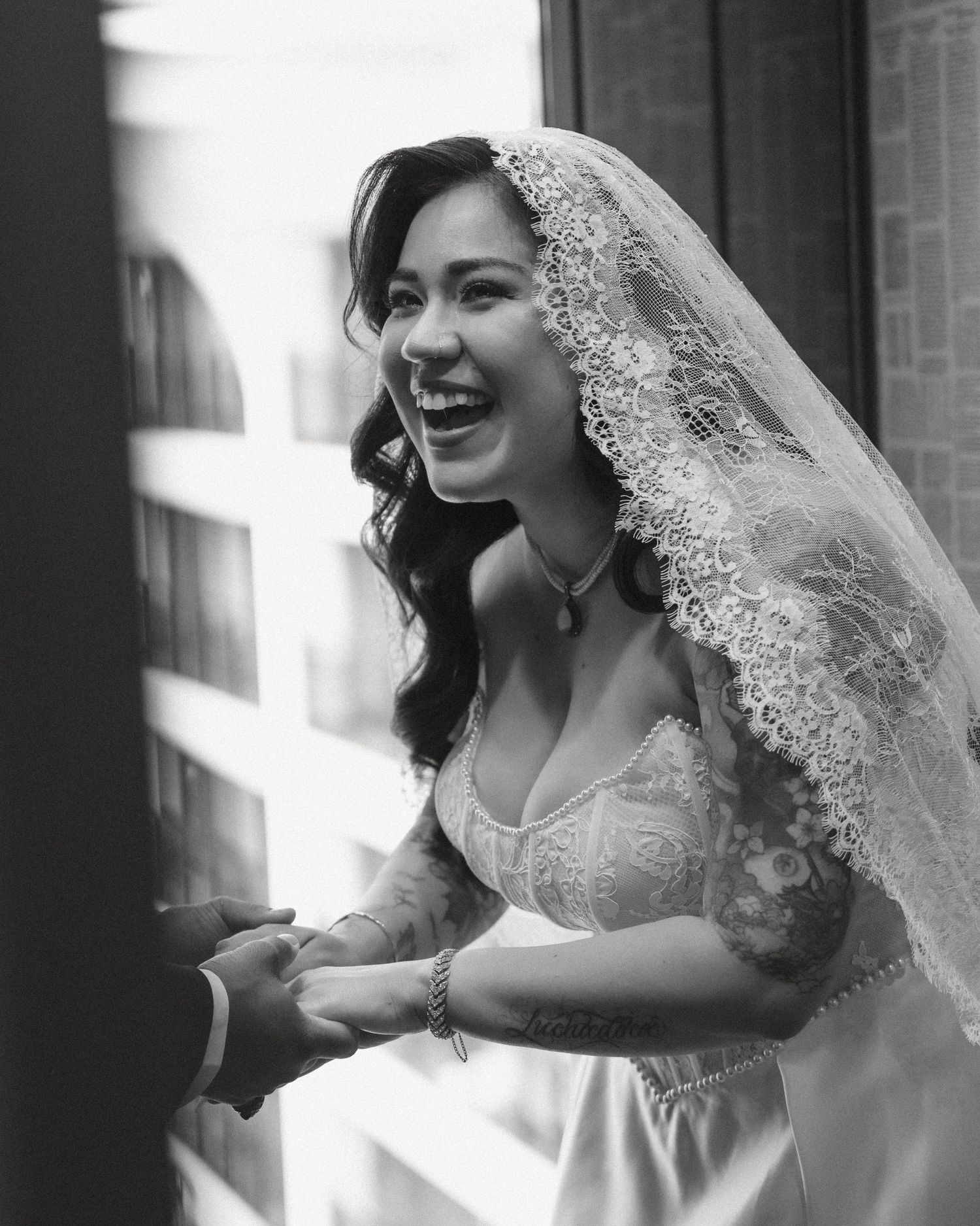 Black and white photo of a joyful bride in lace veil laughing during wedding ceremony.