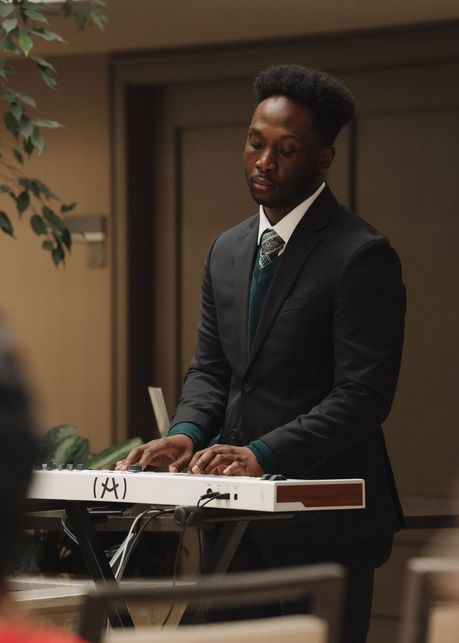 Man in dark suit playing a white keyboard piano at a formal event or venue.