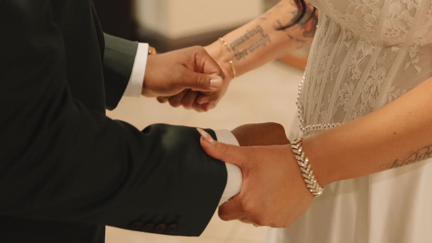 Bride and groom exchanging rings during wedding ceremony, close-up of hands with lace dress and diamond bracelet.
