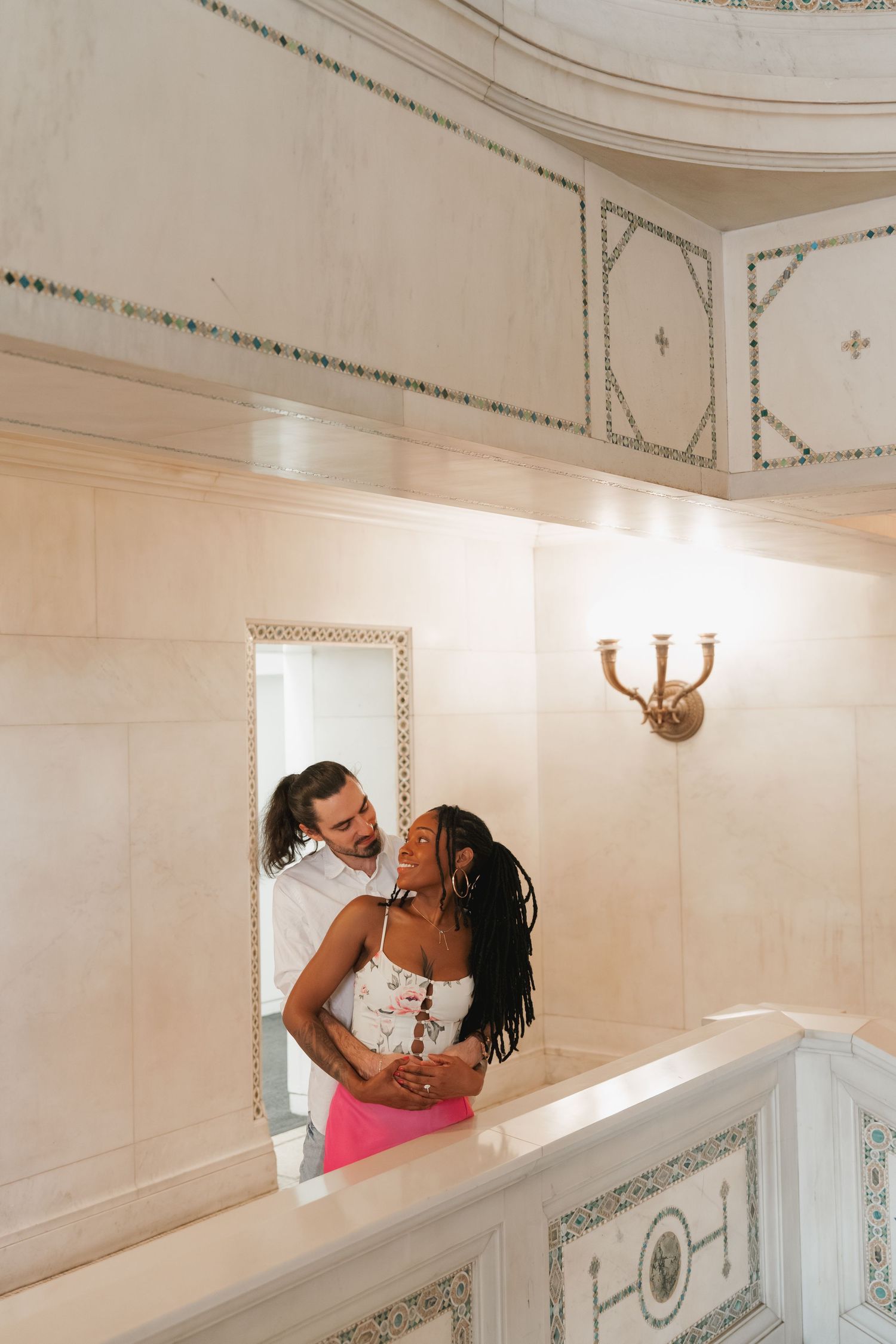 Interracial couple embracing and smiling at each other in a luxurious white marble interior.