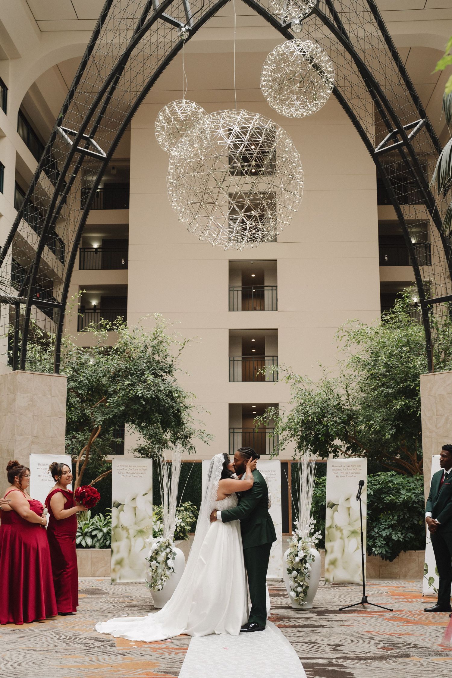 Bride and groom share first kiss under sparkling chandeliers at indoor wedding ceremony.