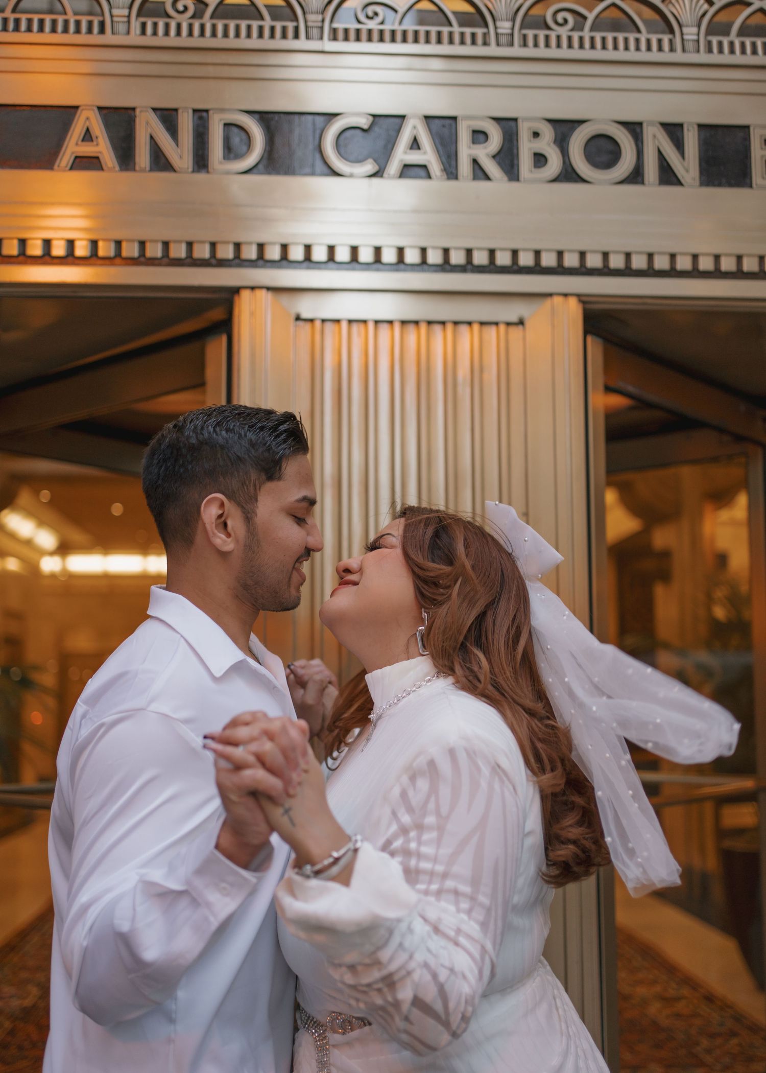 Couple in white wedding attire dancing romantically outside the Carbide and Carbon building in Chicago.