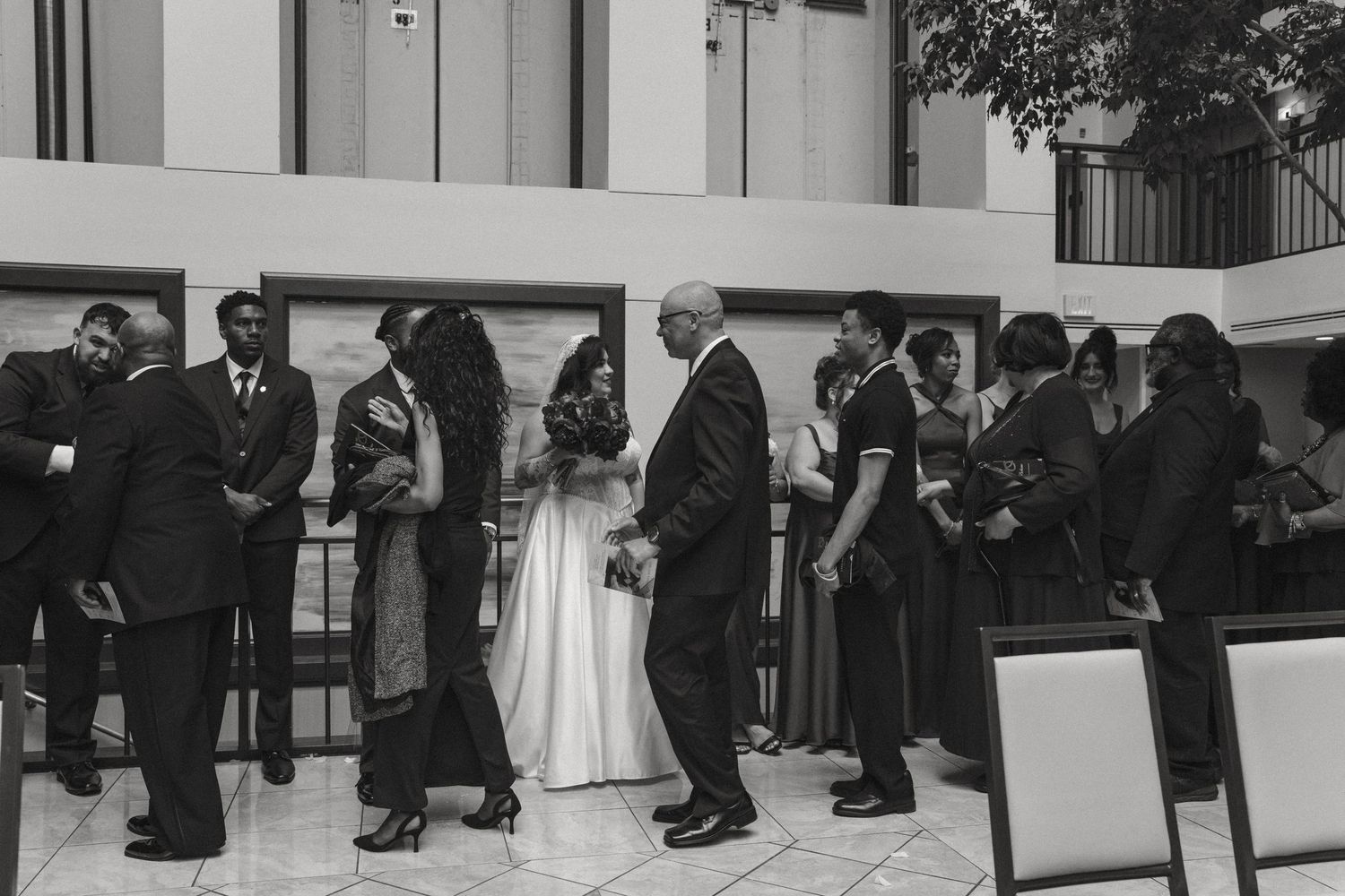 Wedding guests mingle in elegant attire at a formal reception venue in black and white photography.