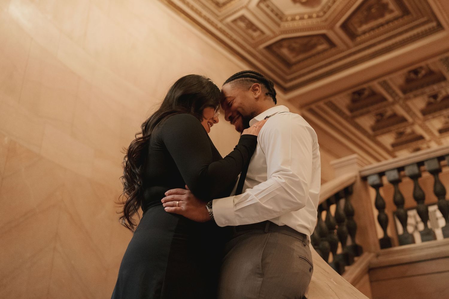 A couple shares a romantic embrace near an elegant staircase in a grand ornate building, Chicago Cultural Center.
