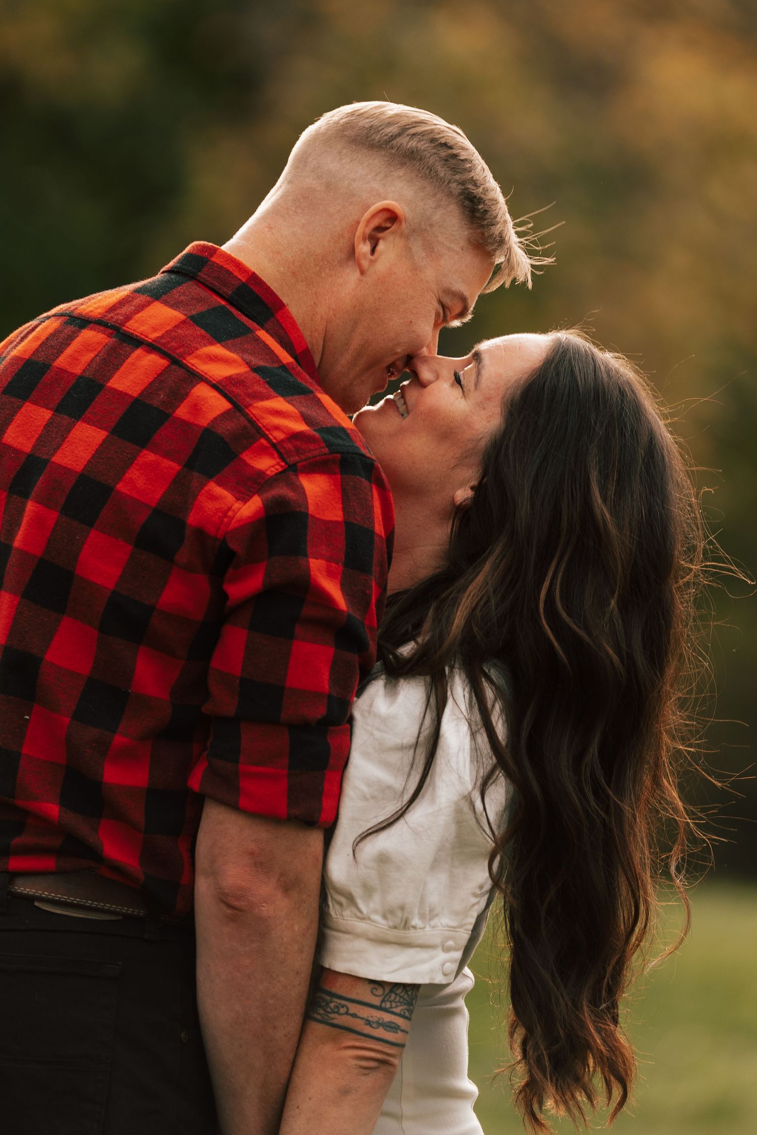 Couple sharing a tender almost-kiss outdoors, man in red plaid shirt and woman with long dark hair.