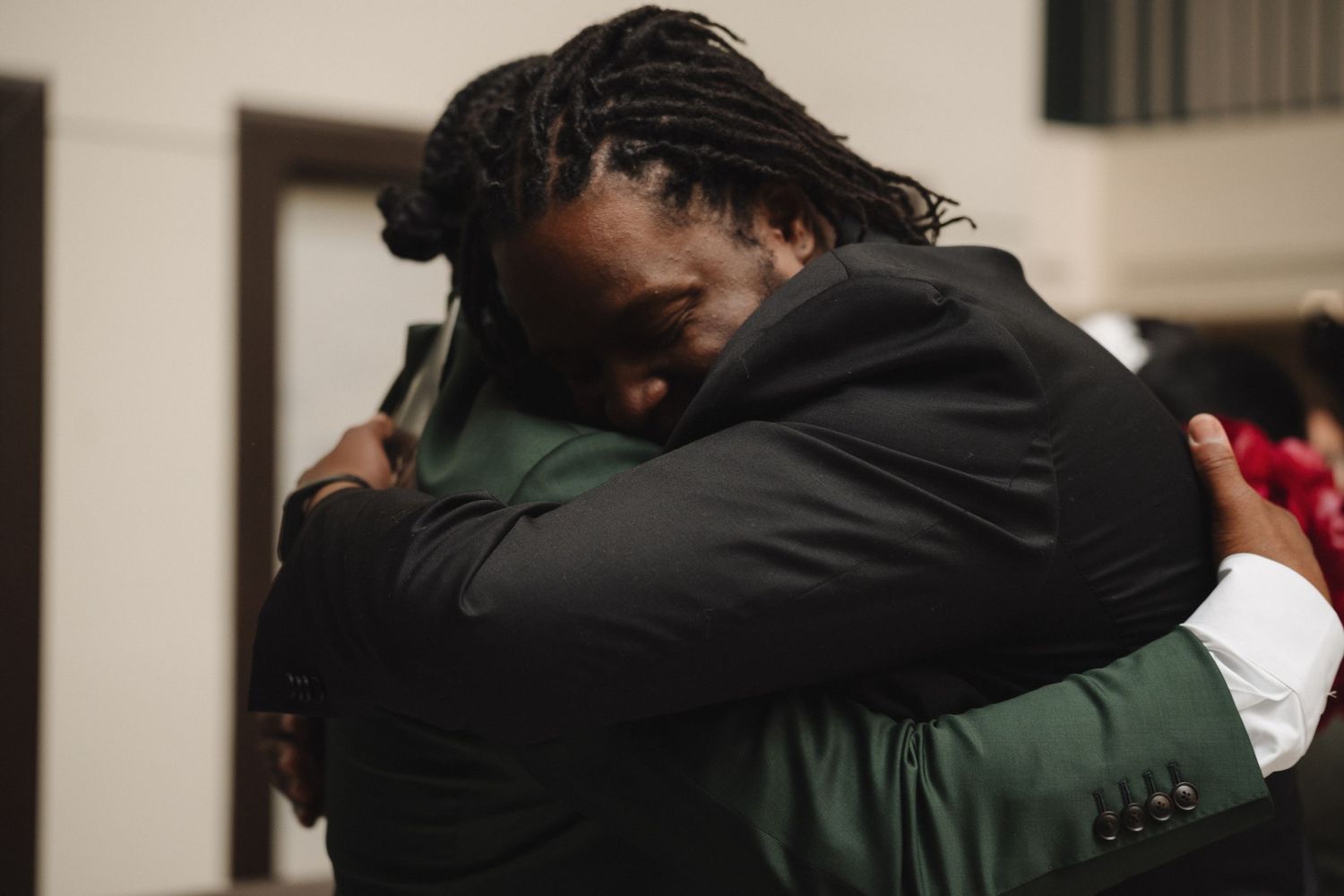 Two men share an emotional embrace at a wedding celebration wearing formal suits.