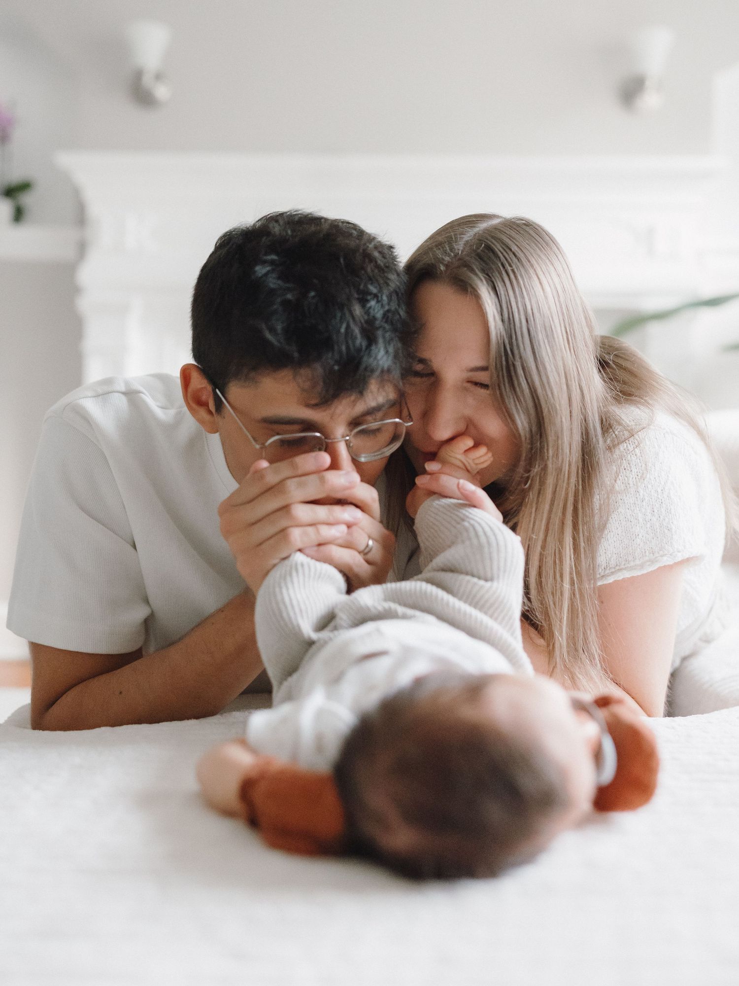 Young parents lying on couch smiling and holding their newborn baby's tiny feet together.