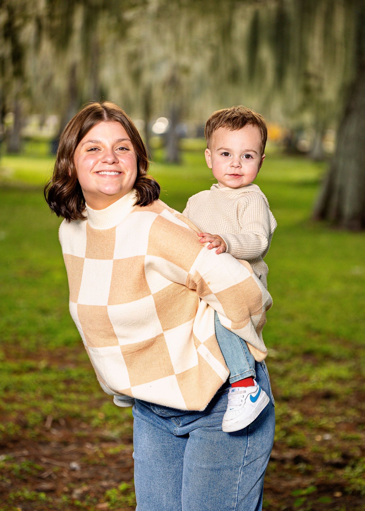 Family portrait session outdoors with matching checkered sweaters in park setting.
